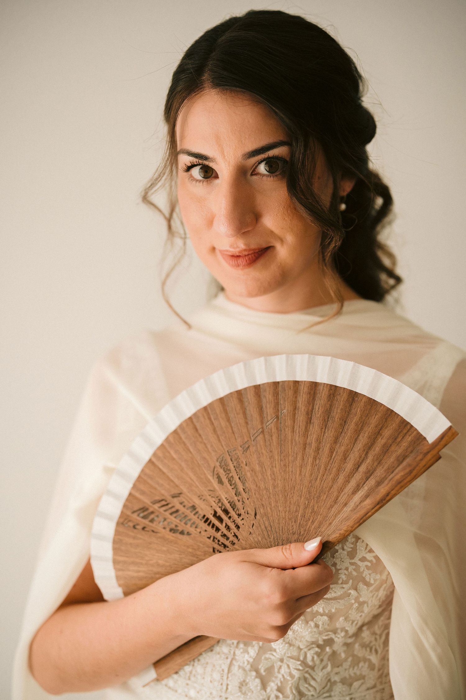 Elegant wedding portrait featuring a traditional wooden hand fan and delicate white dress with romantic styling.