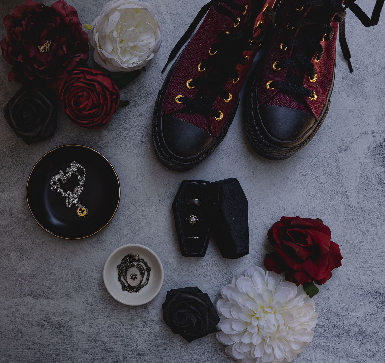 Flat lay of red and black sneakers with roses and wedding accessories on grey surface.