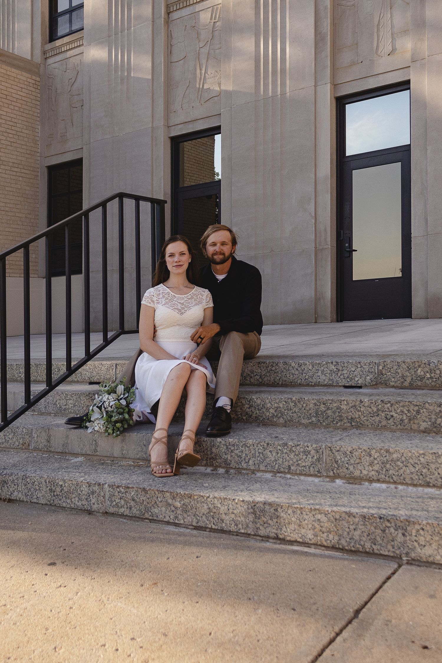 Couple sitting together on grand stone steps of a historic building.
