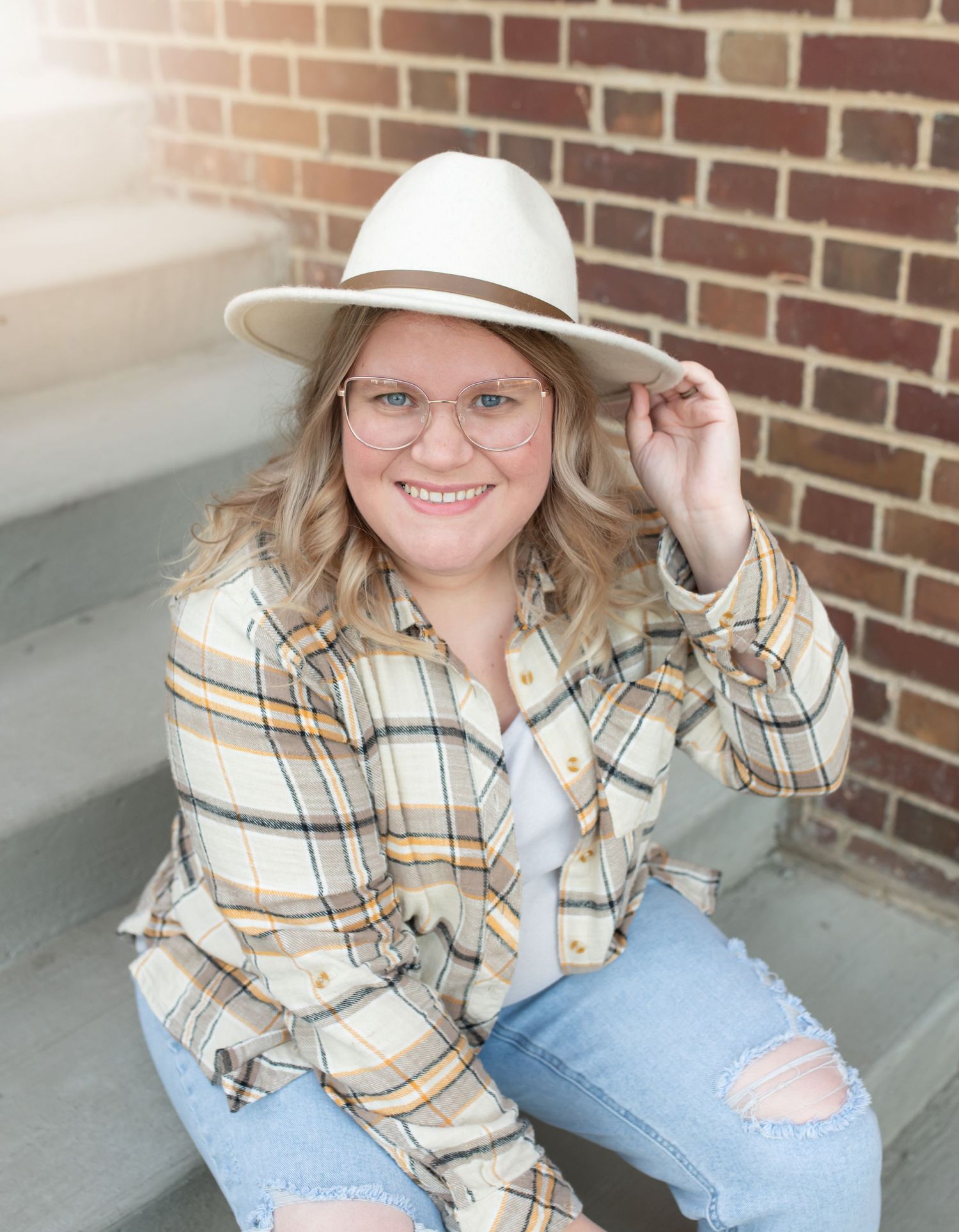 Person in plaid shirt and white hat sitting on brick steps with casual style.