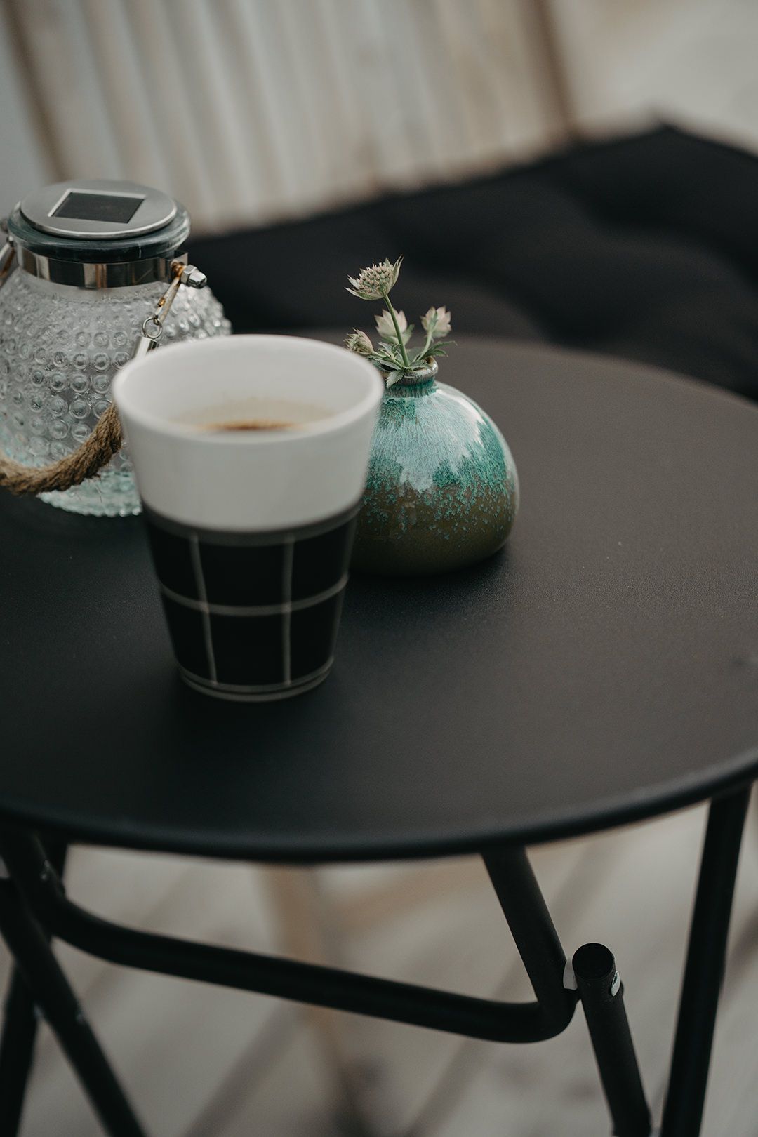 Minimalist black coffee table setup with white ceramic mugs and small turquoise vase on dark surface in moody lighting.