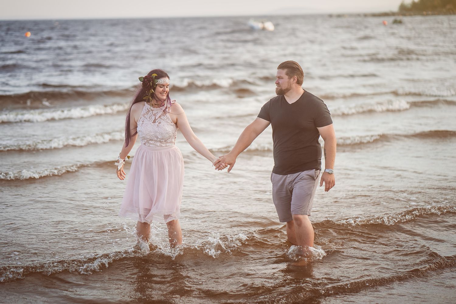 Couple holding hands while wading in ocean waves at sunset.
