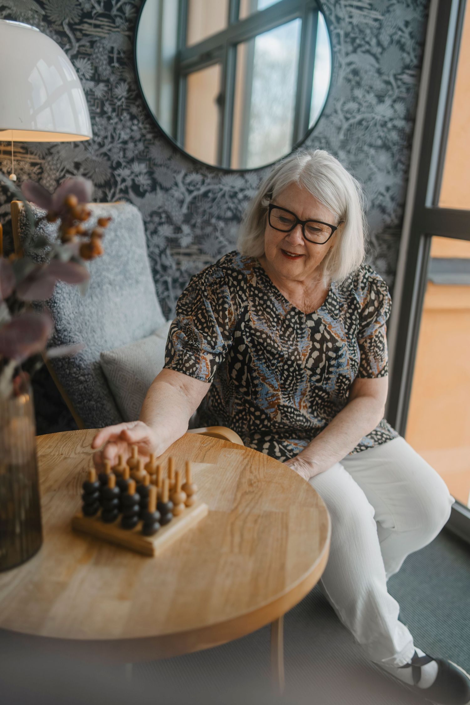 Someone in a patterned shirt sits at a wooden table with a chess set.