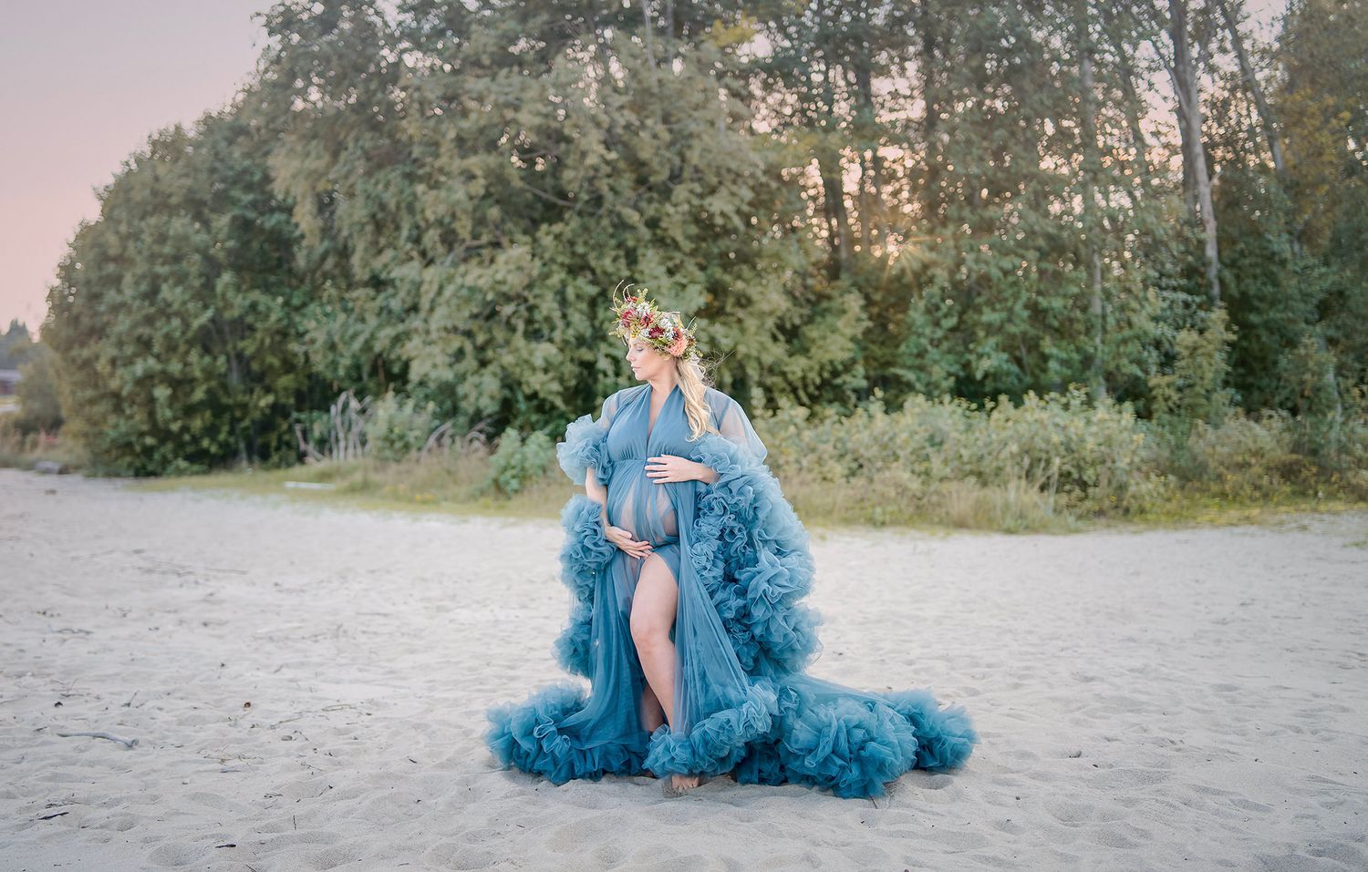 A ethereal blue tulle gown flows dramatically against a misty beach setting with trees in the background.