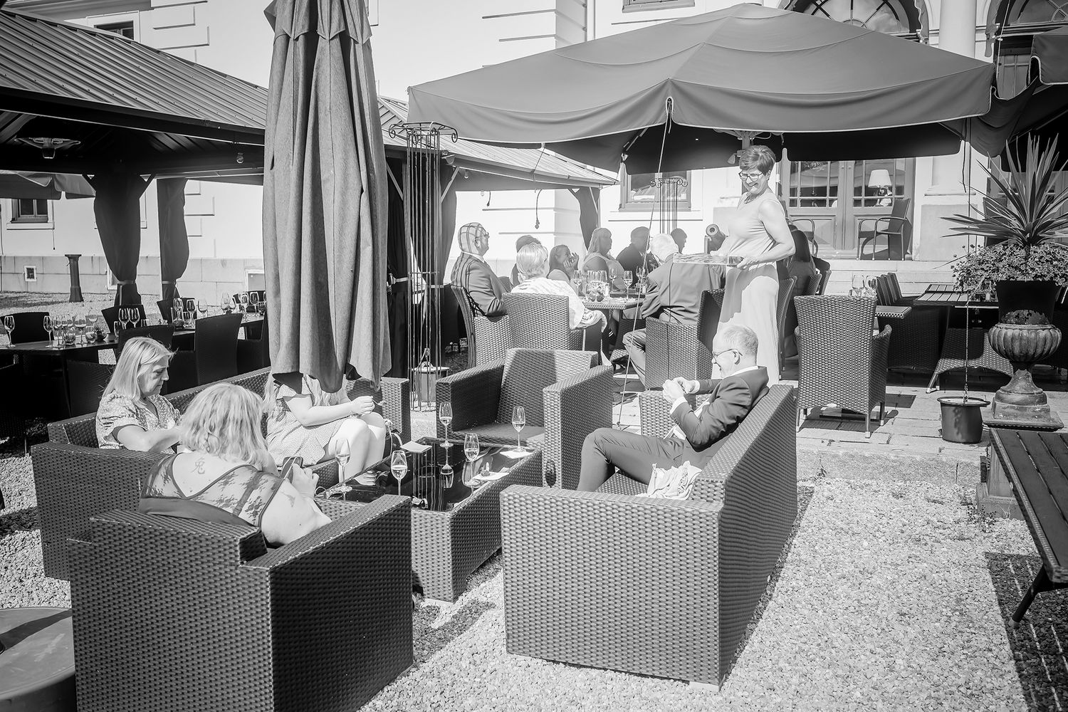 Black and white photo of diners enjoying outdoor patio seating with wicker furniture and umbrellas at a cafe restaurant.