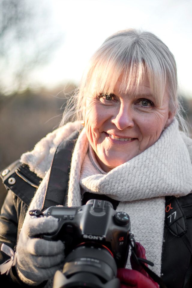 Photographer with Sony camera wearing winter scarf and gloves during golden hour.