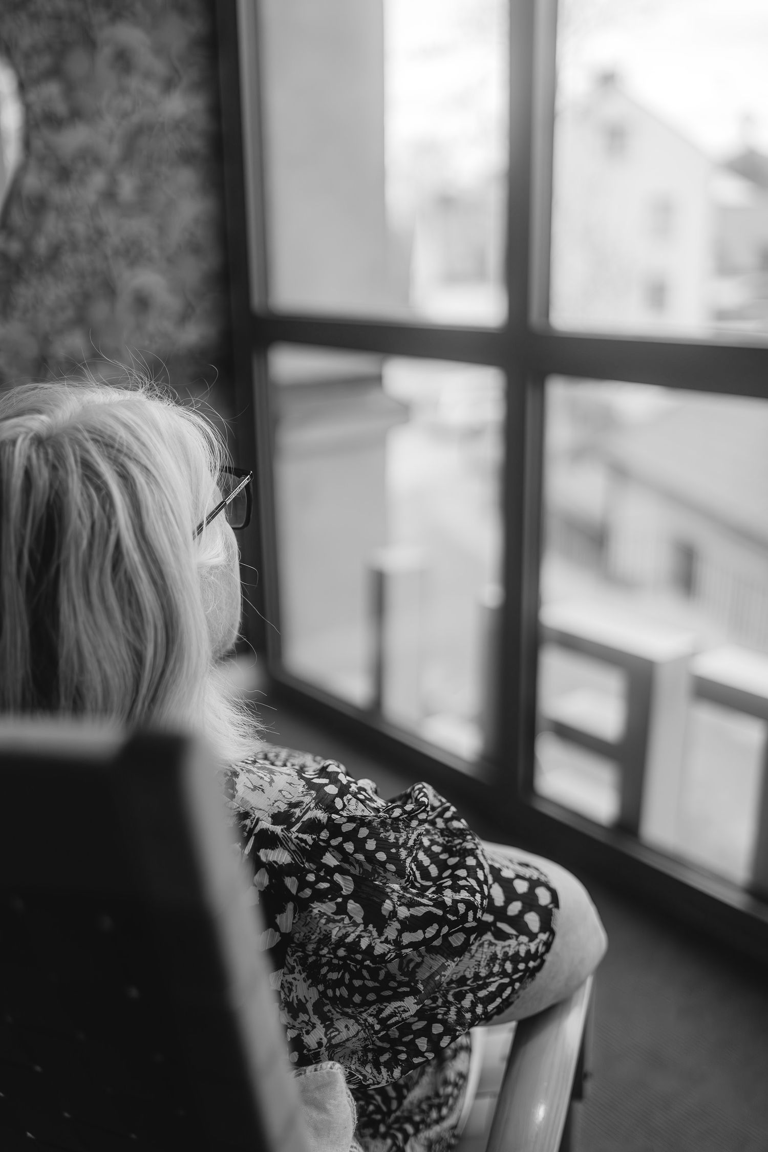 A person gazing out of a window in black and white photography.