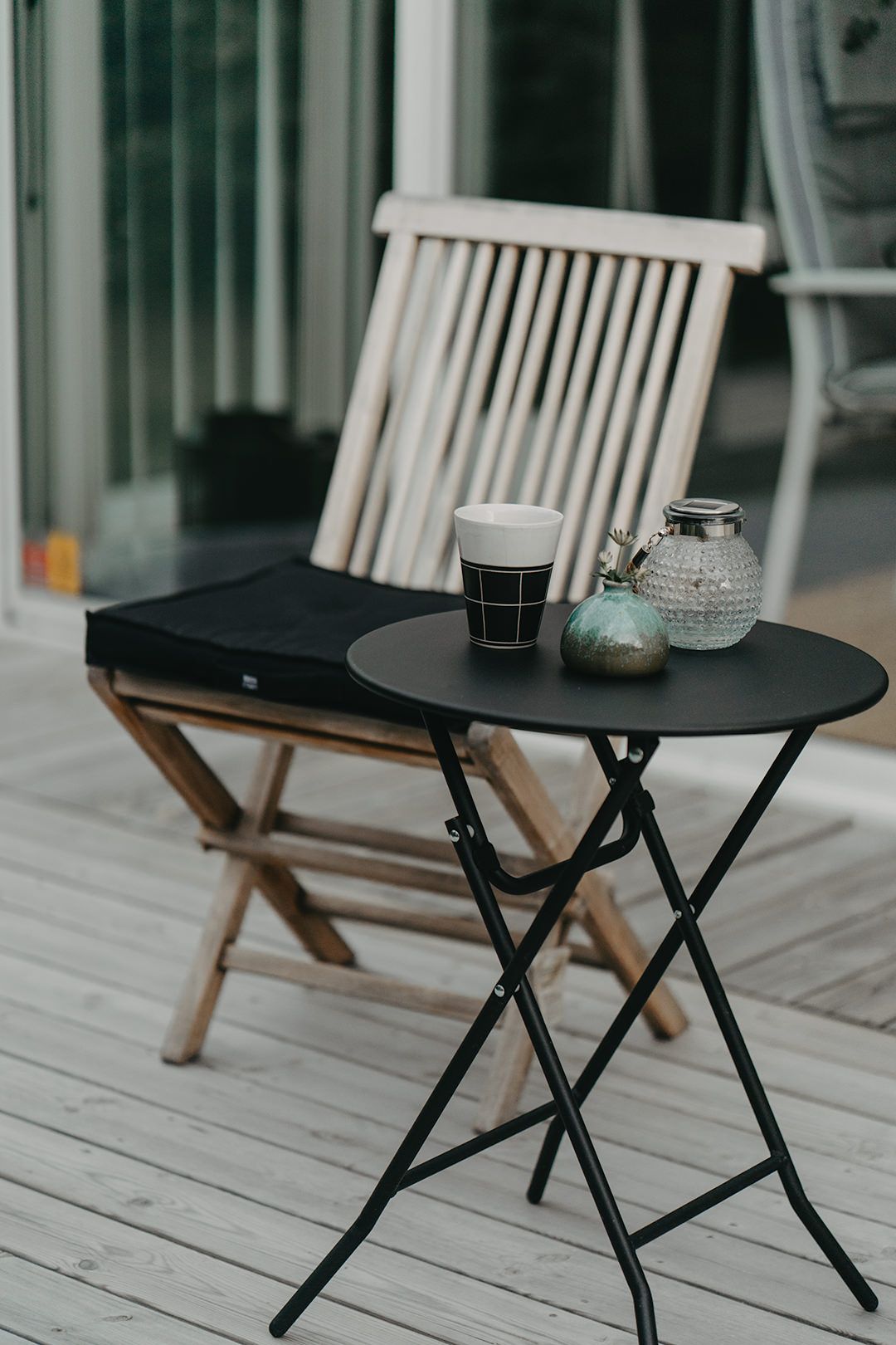 Black modern coffee table and folding wooden chairs on a white deck create a minimalist outdoor seating arrangement.