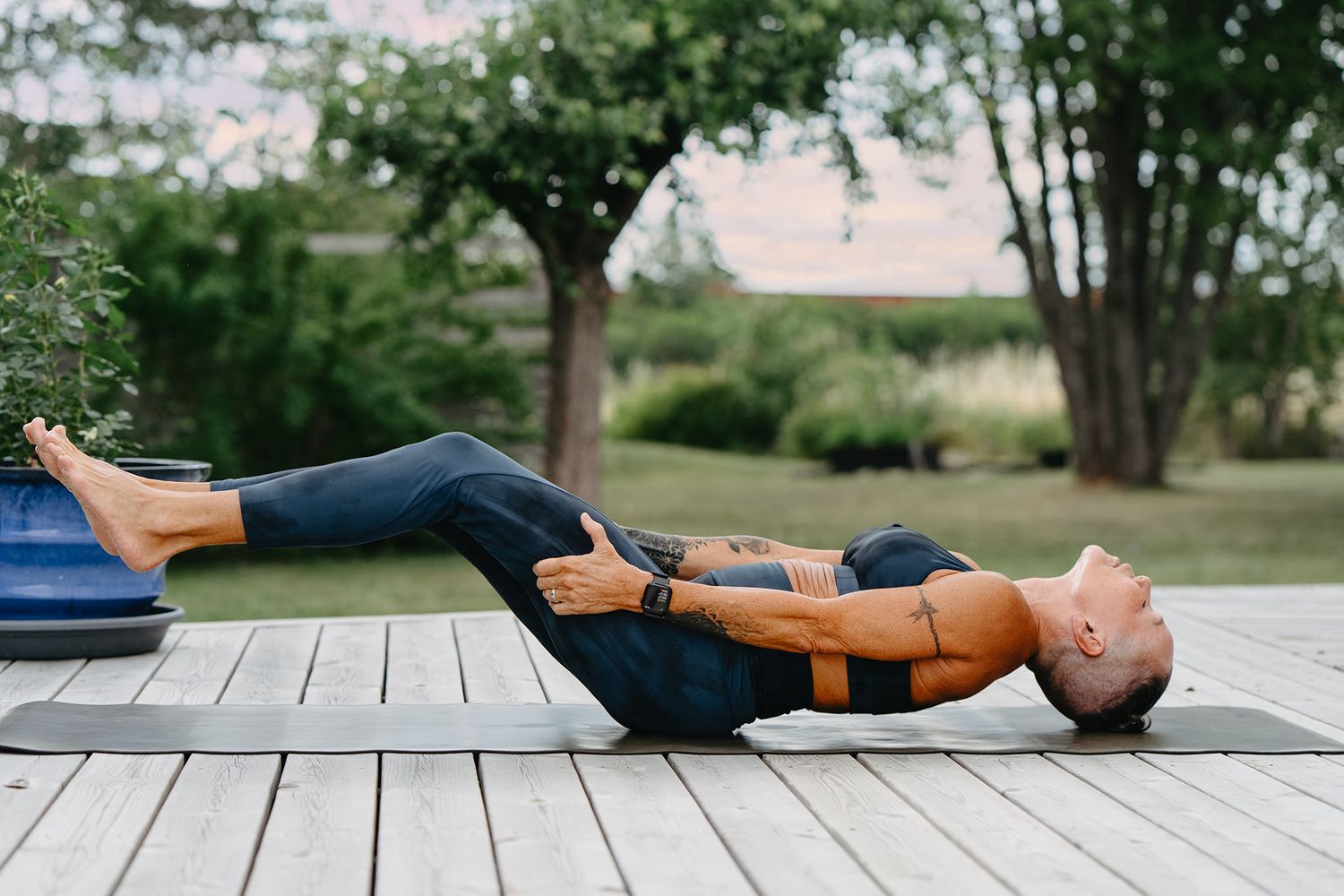 Person lying on wooden deck practicing progressive relaxation exercises in a peaceful outdoor garden setting.