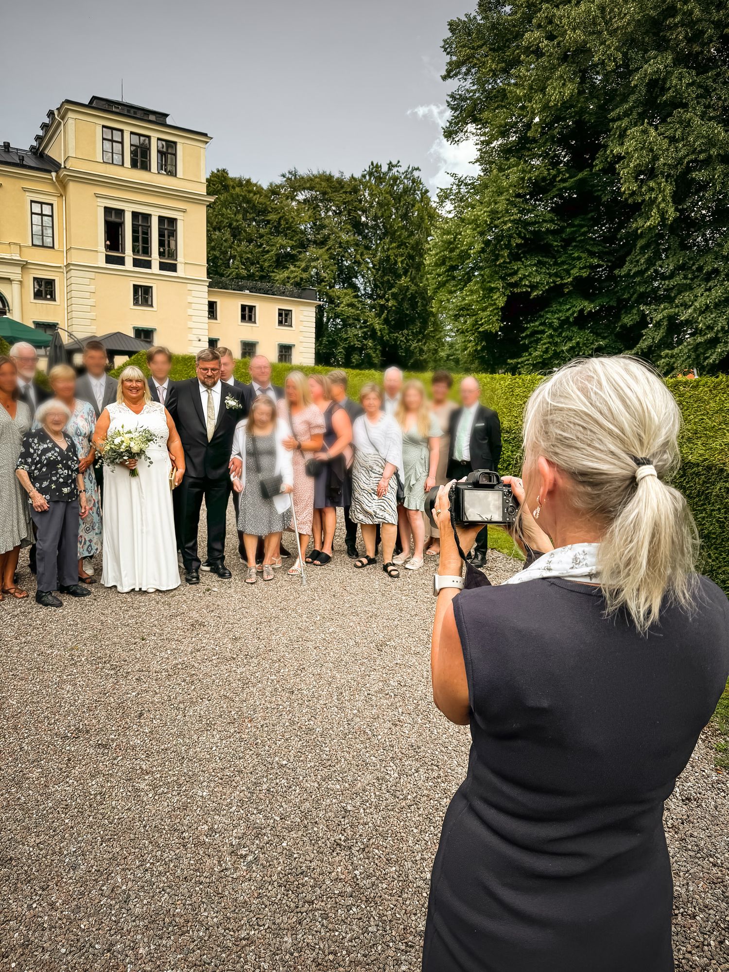 Wedding photographer captures group photo of guests outside yellow mansion.