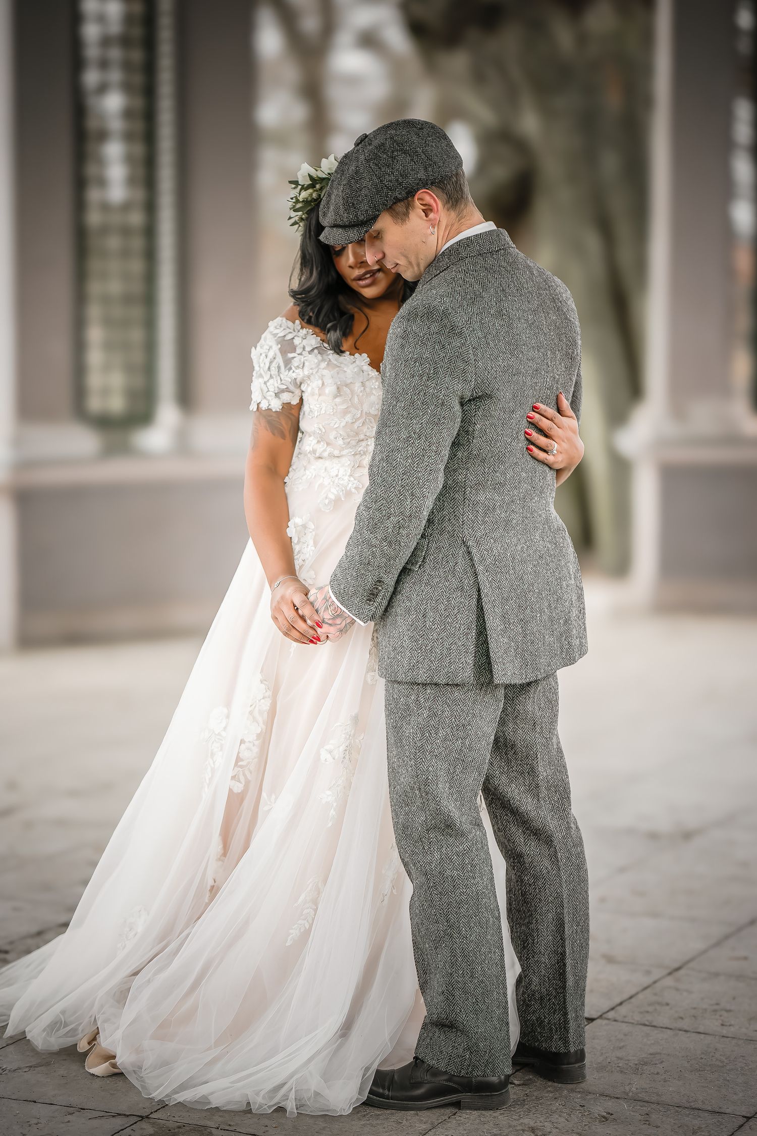 Tender moment between couple in vintage-inspired gray suit and lace wedding gown.