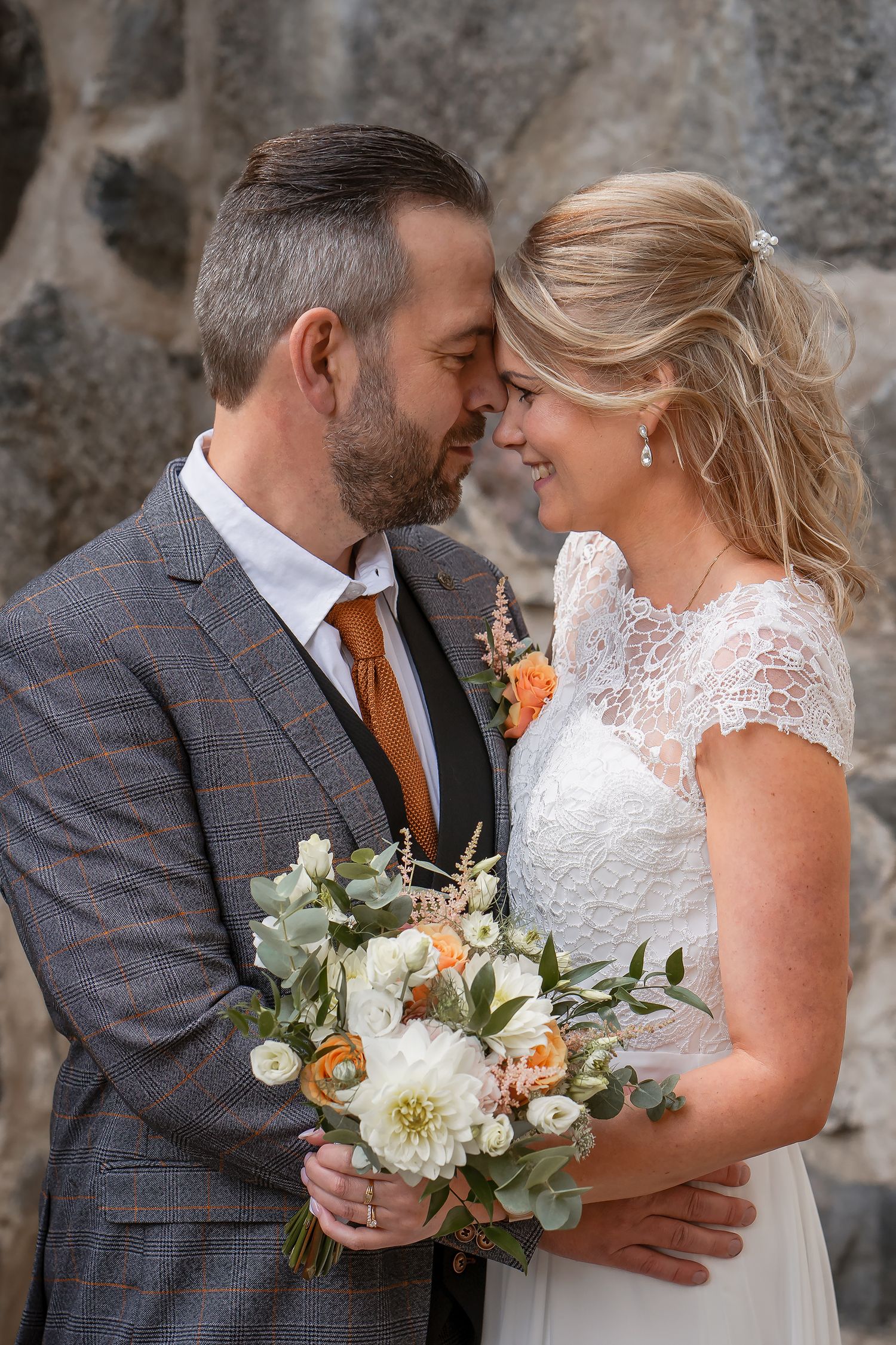 A wedding couple shares an intimate moment while holding a white and peach floral bouquet.