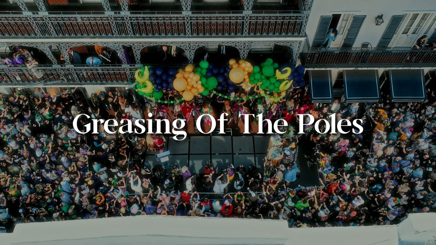 Large crowd gathered beneath colorful balloons during a festive Mardi Gras celebration.
