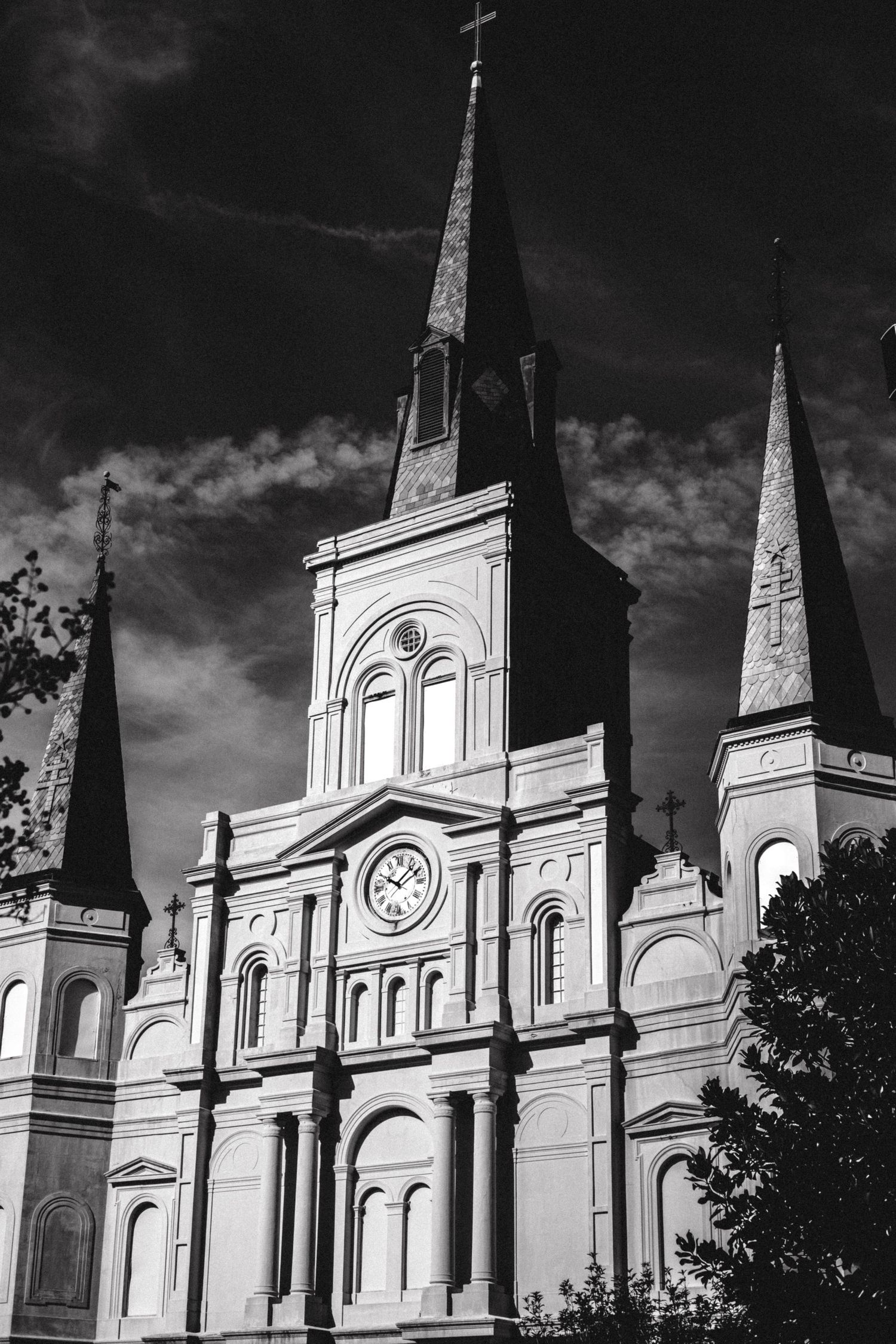 Dramatic black and white view of St. Louis Cathedral's iconic spires against cloudy sky.