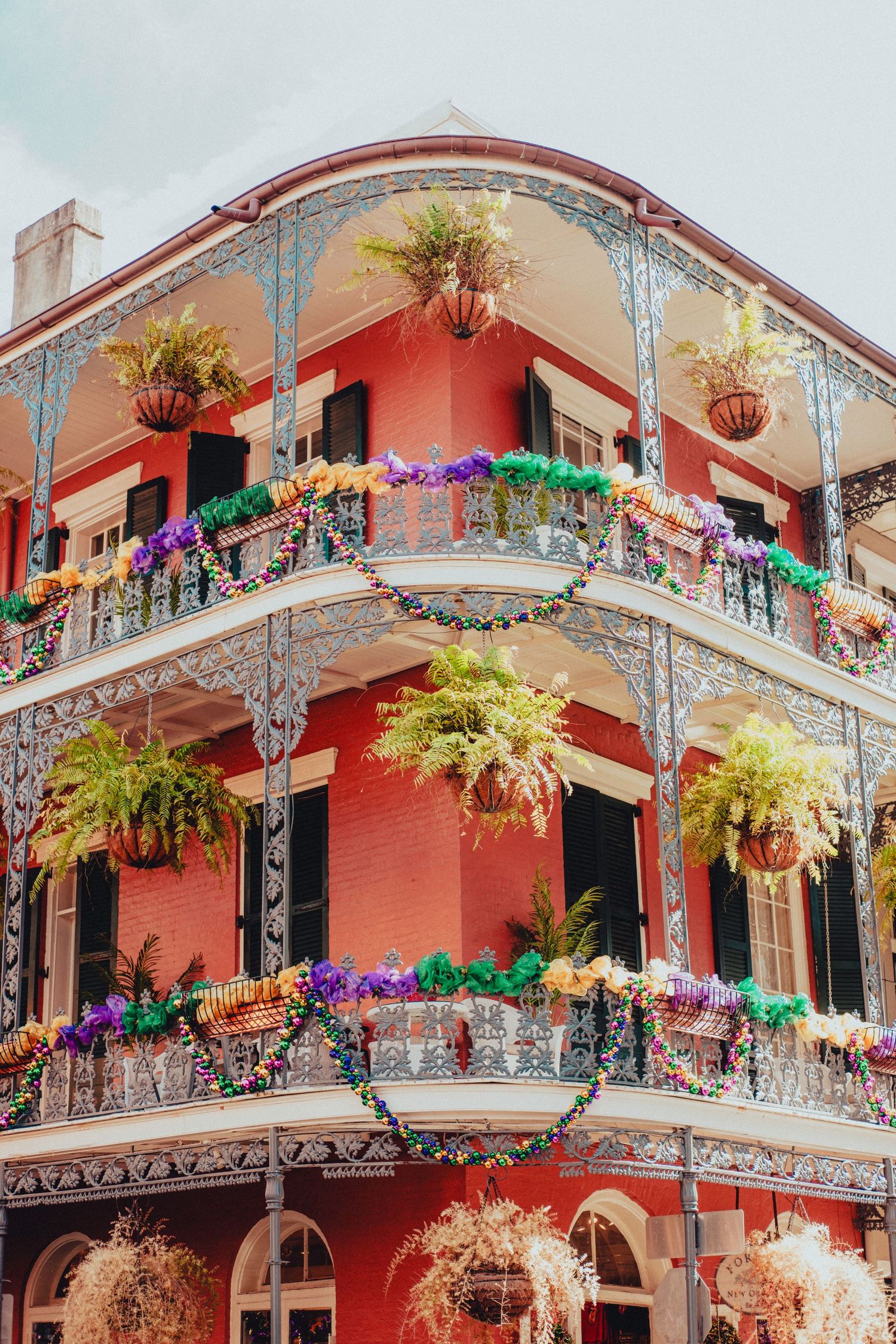 Colorful French Quarter balcony decorated with hanging plants and Mardi Gras decorations in New Orleans.