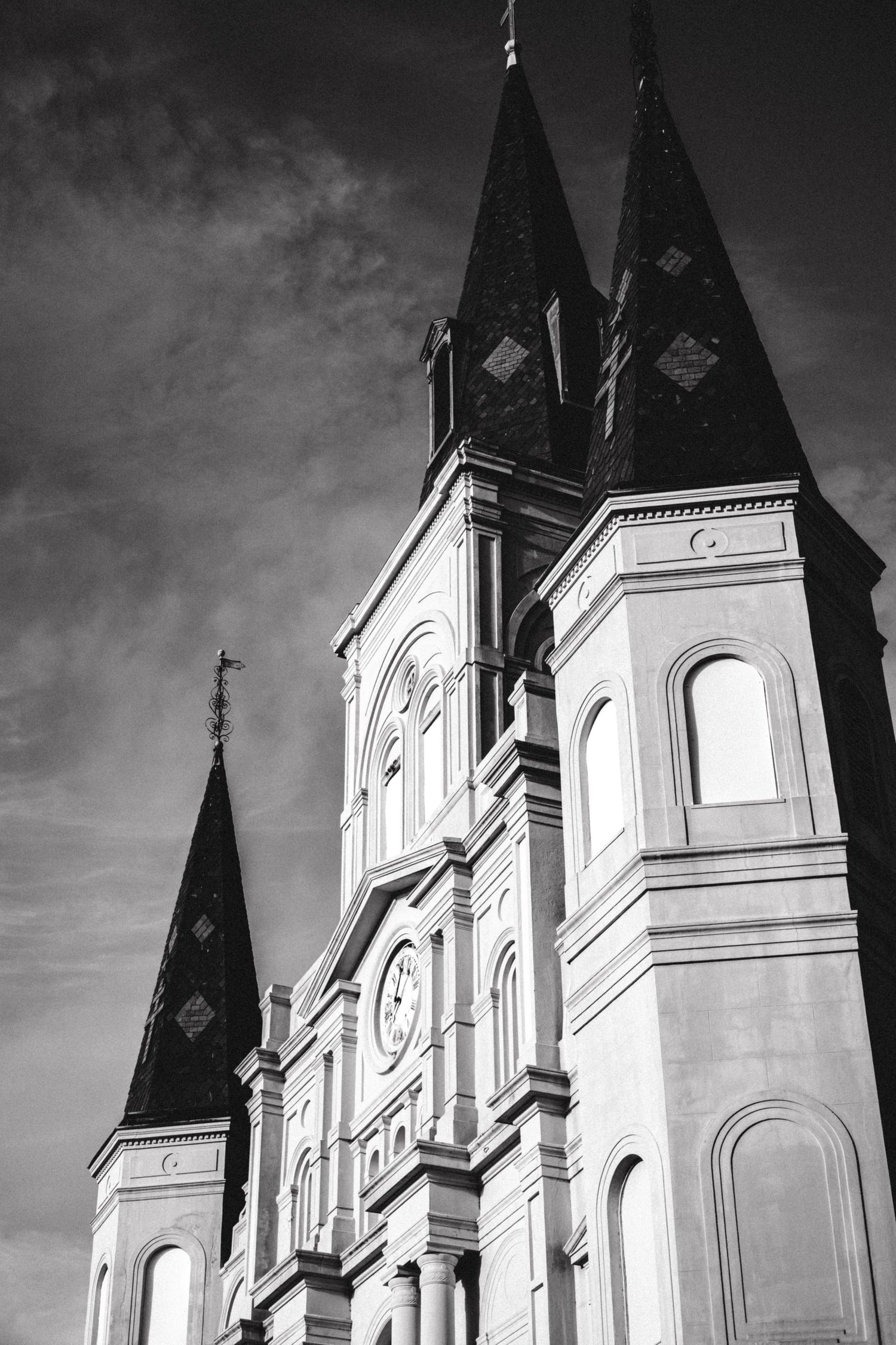 Black and white architectural photo of gothic church spires against cloudy sky.