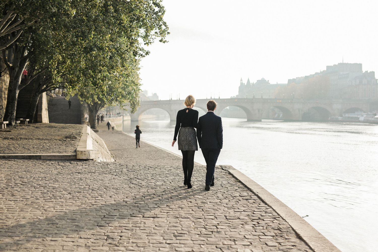 Engagement shoot in Paris with couple walking in the sunrise along the river