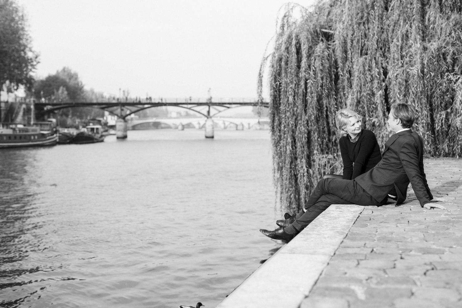 Couple sitting down by the river and enjoying each other's company in Paris in the sunrise for their engagement shoot