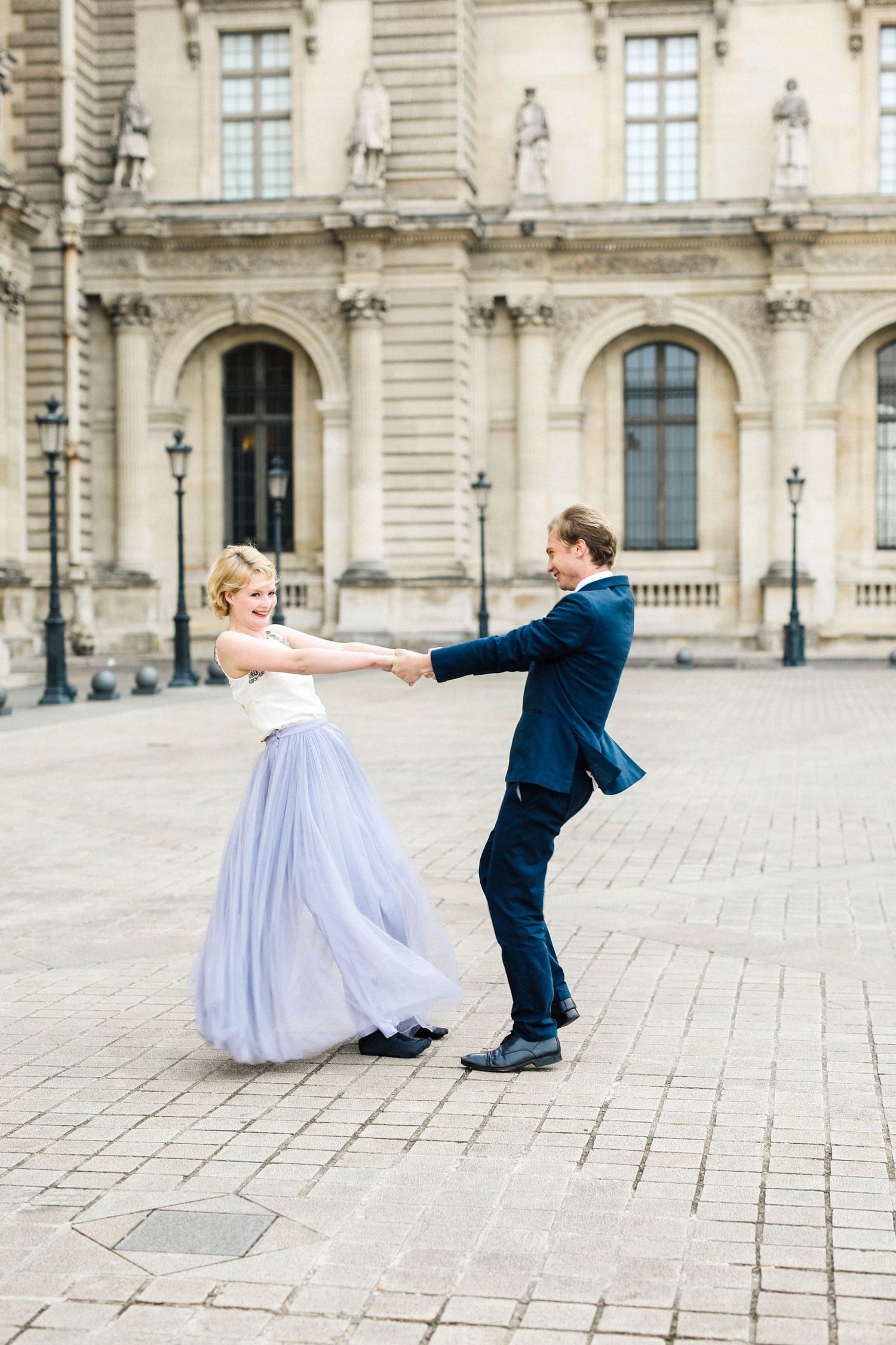 Couple playfully posing in the Louvre in Paris in the sunrise for their engagement shoot