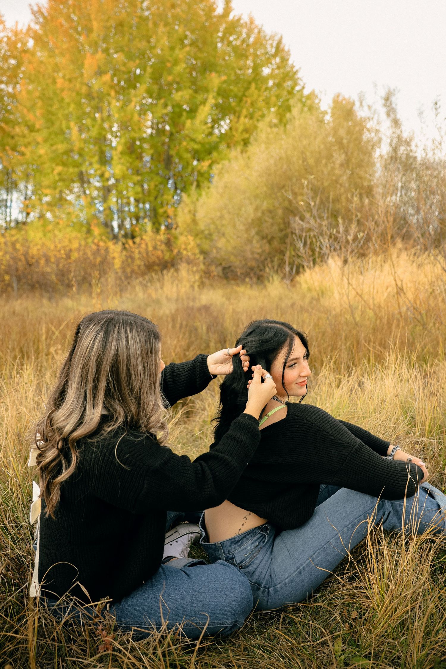 Two people sitting in autumn field while one styles the other's hair during sunset.