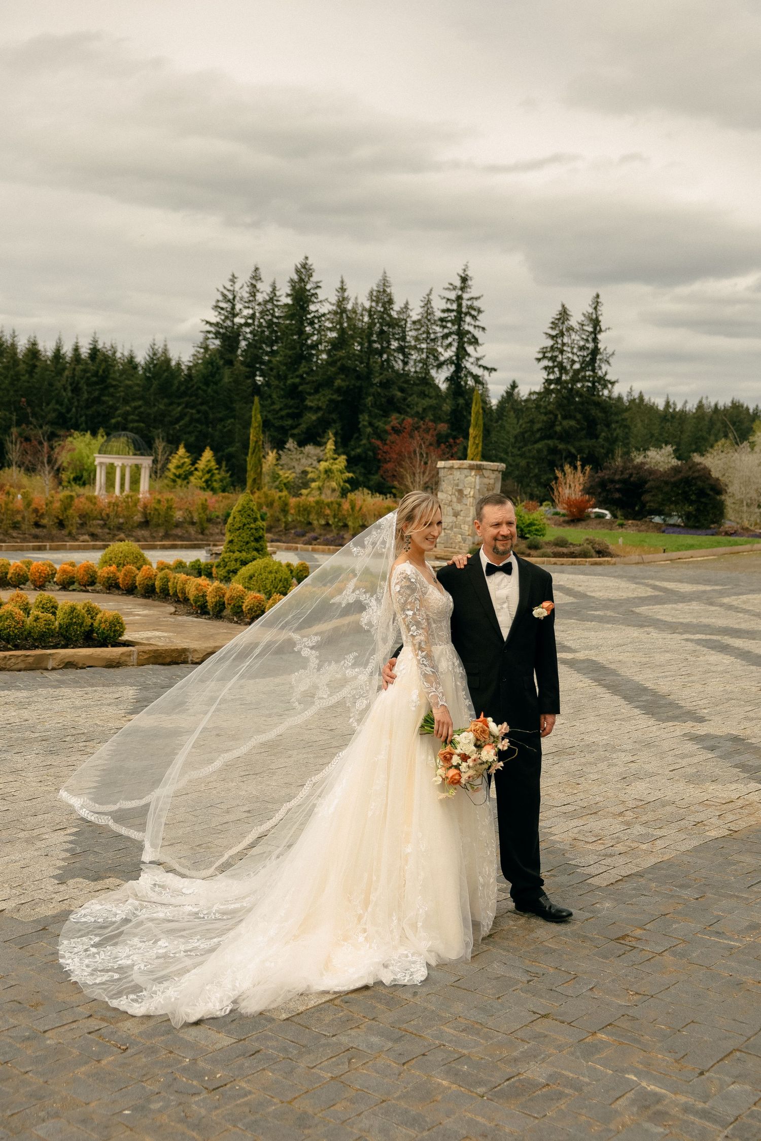 Elegant bride and groom portrait on stone pathway with dramatic cloudy sky backdrop.