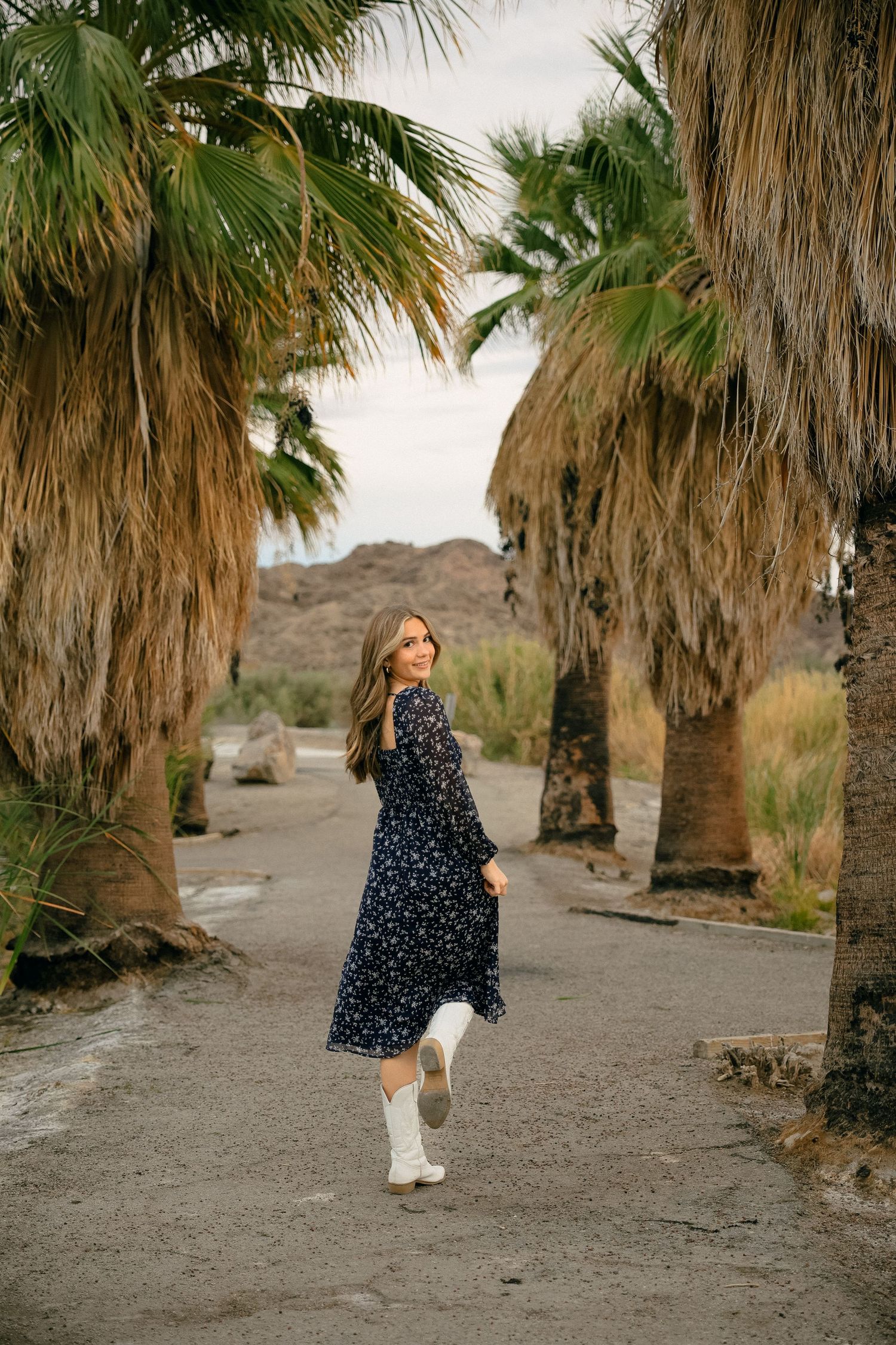 Person in polka dot dress twirls between palm trees on desert path.