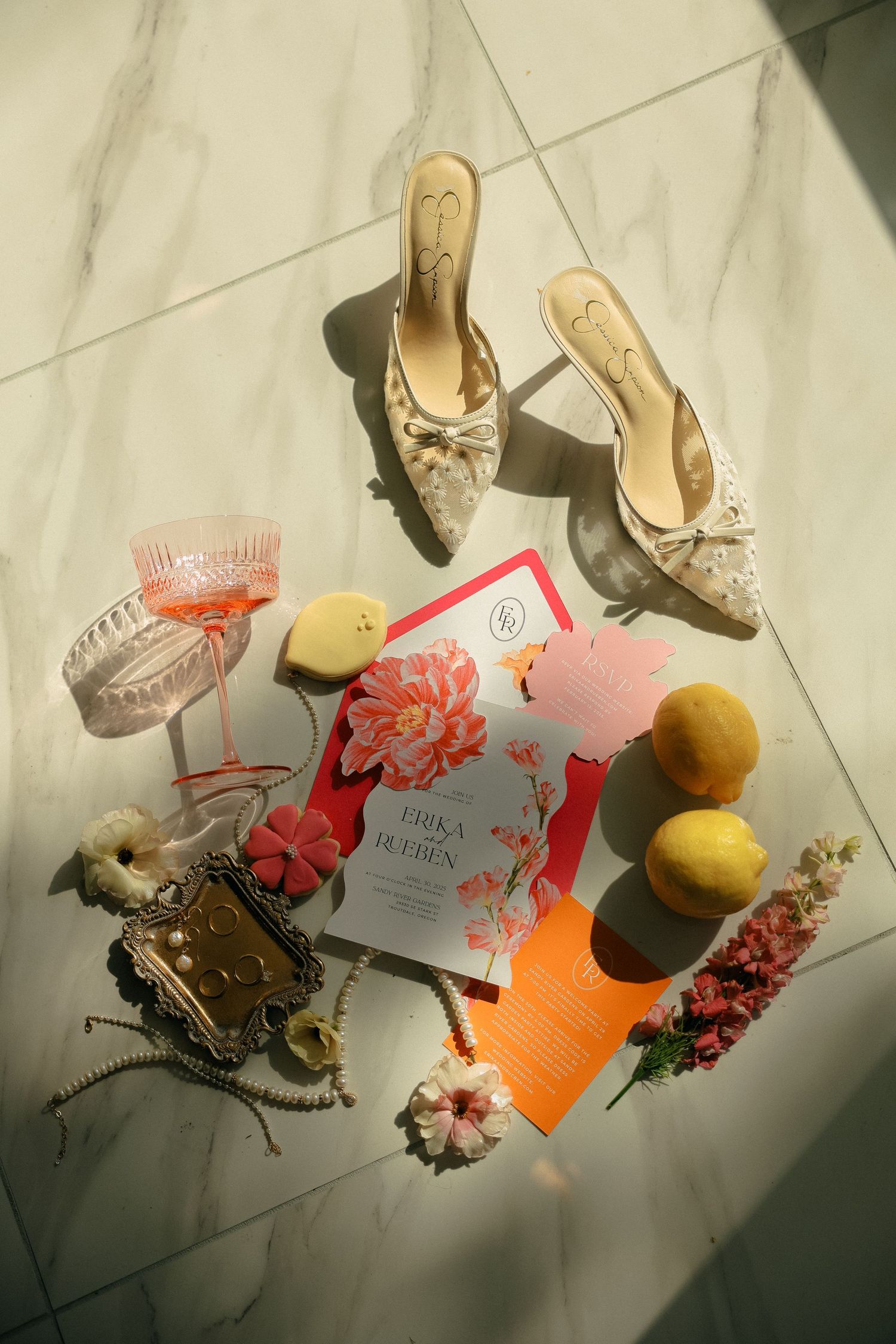 Wedding details flat lay with elegant shoes, invitations, lemons and flowers on marble flooring.