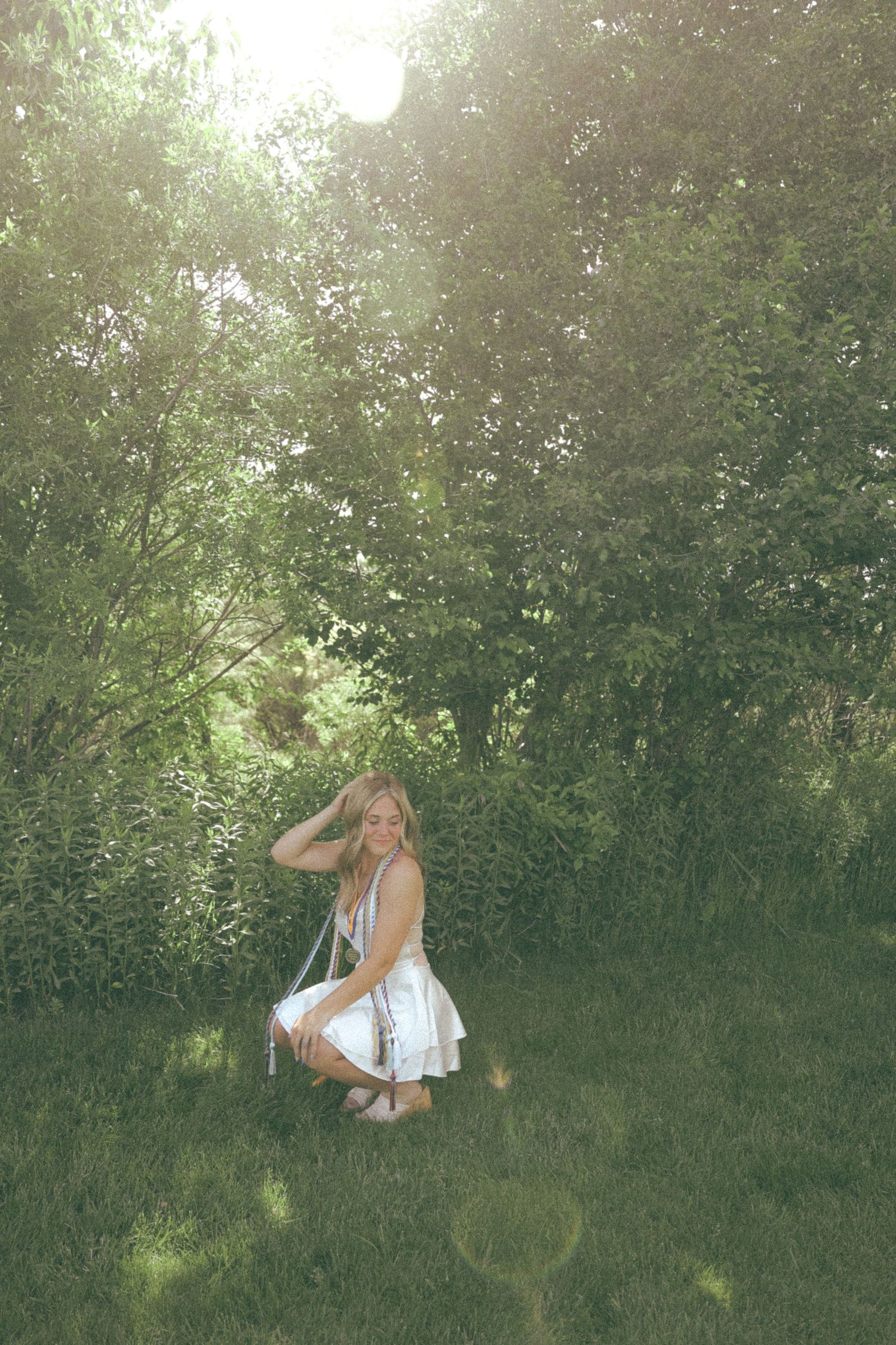 Dreamy garden portrait in white dress with sunlight filtering through trees.