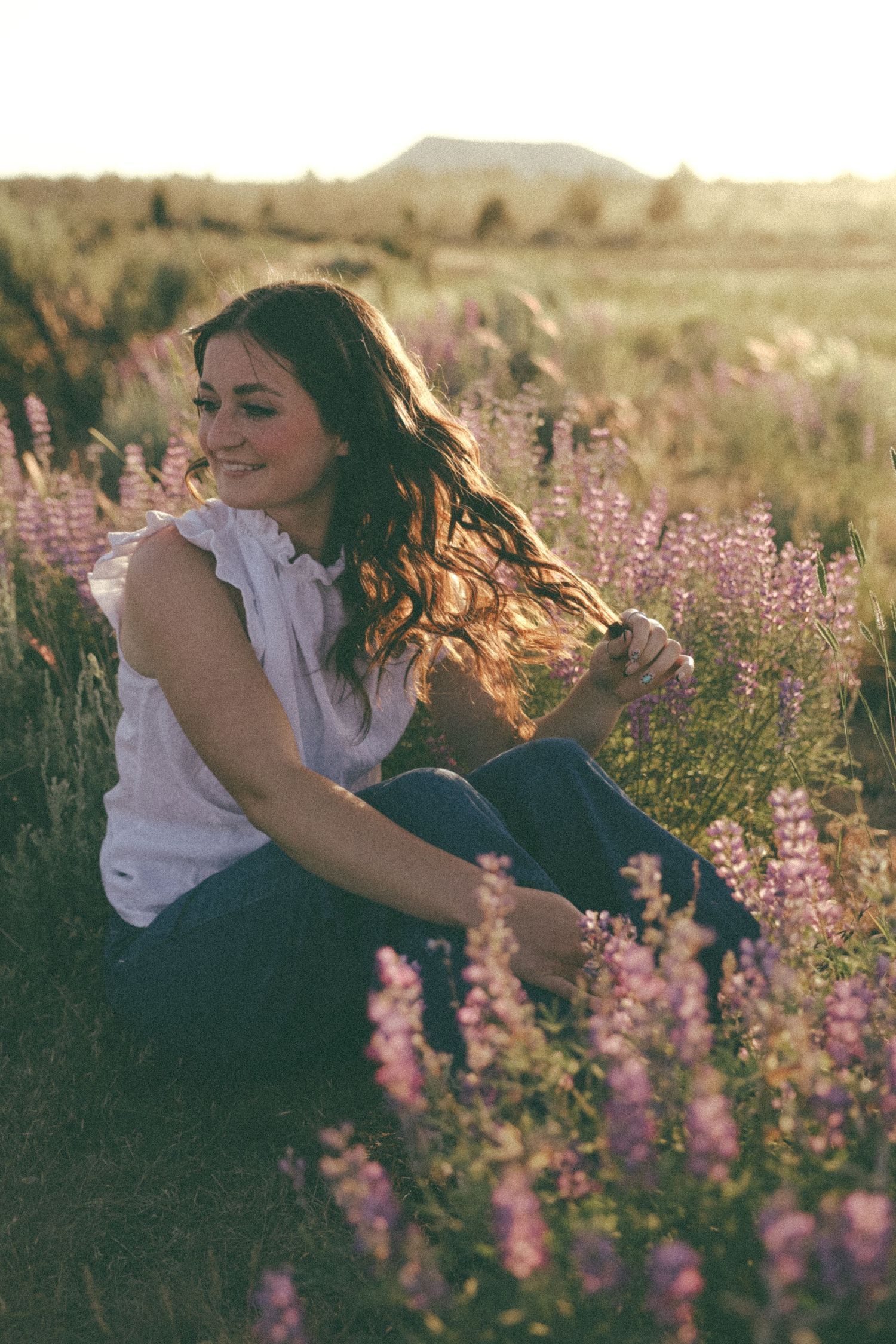 A person sits among blooming purple lupine flowers in a meadow during golden hour.