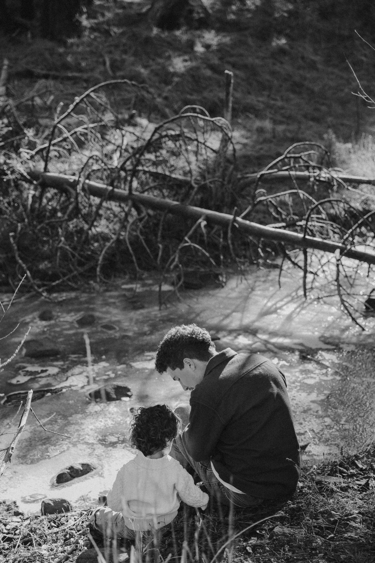 A tender moment between parent and child sitting by a stream in black and white.