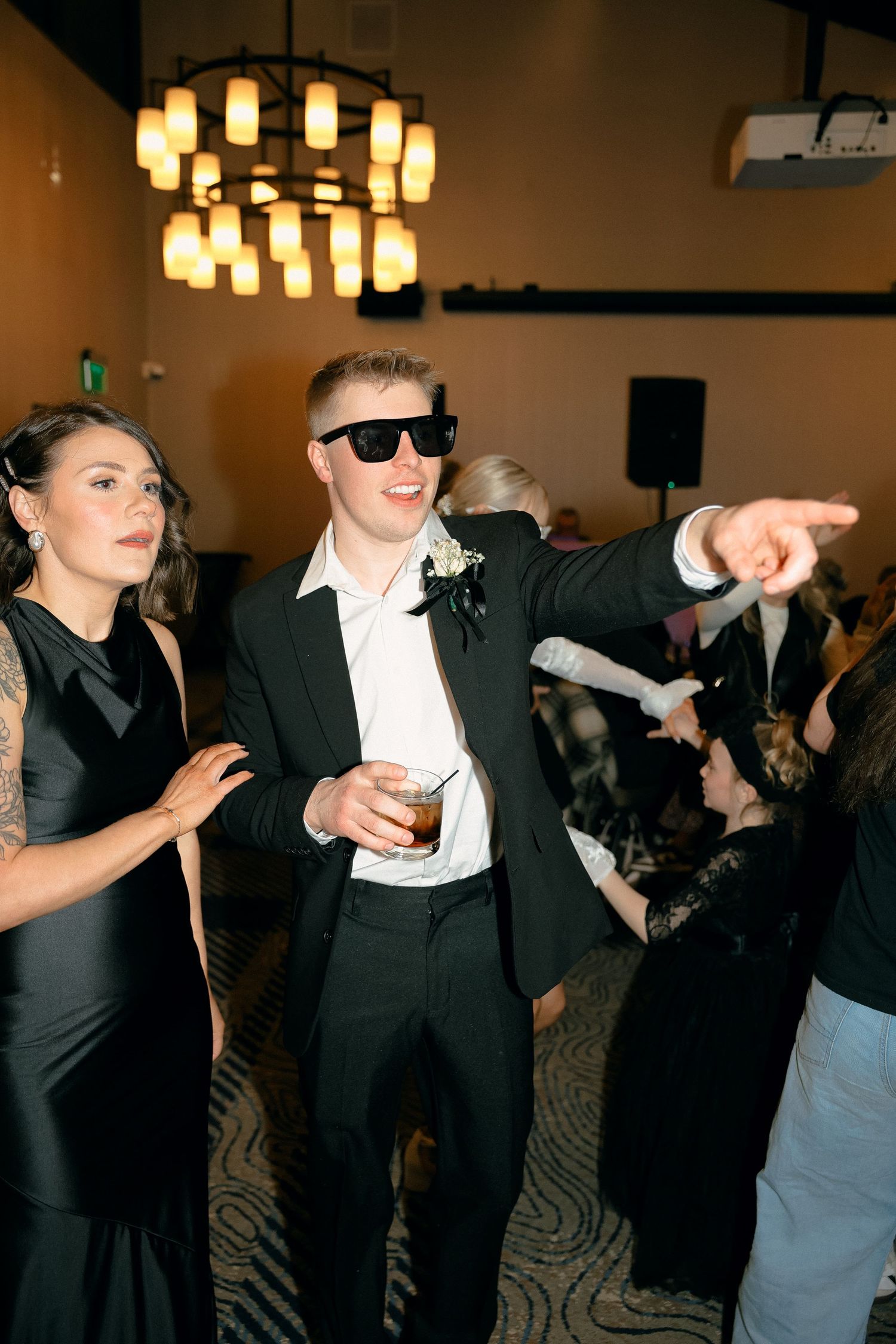 Wedding guests in formal attire dancing energetically at a reception with dramatic lighting.