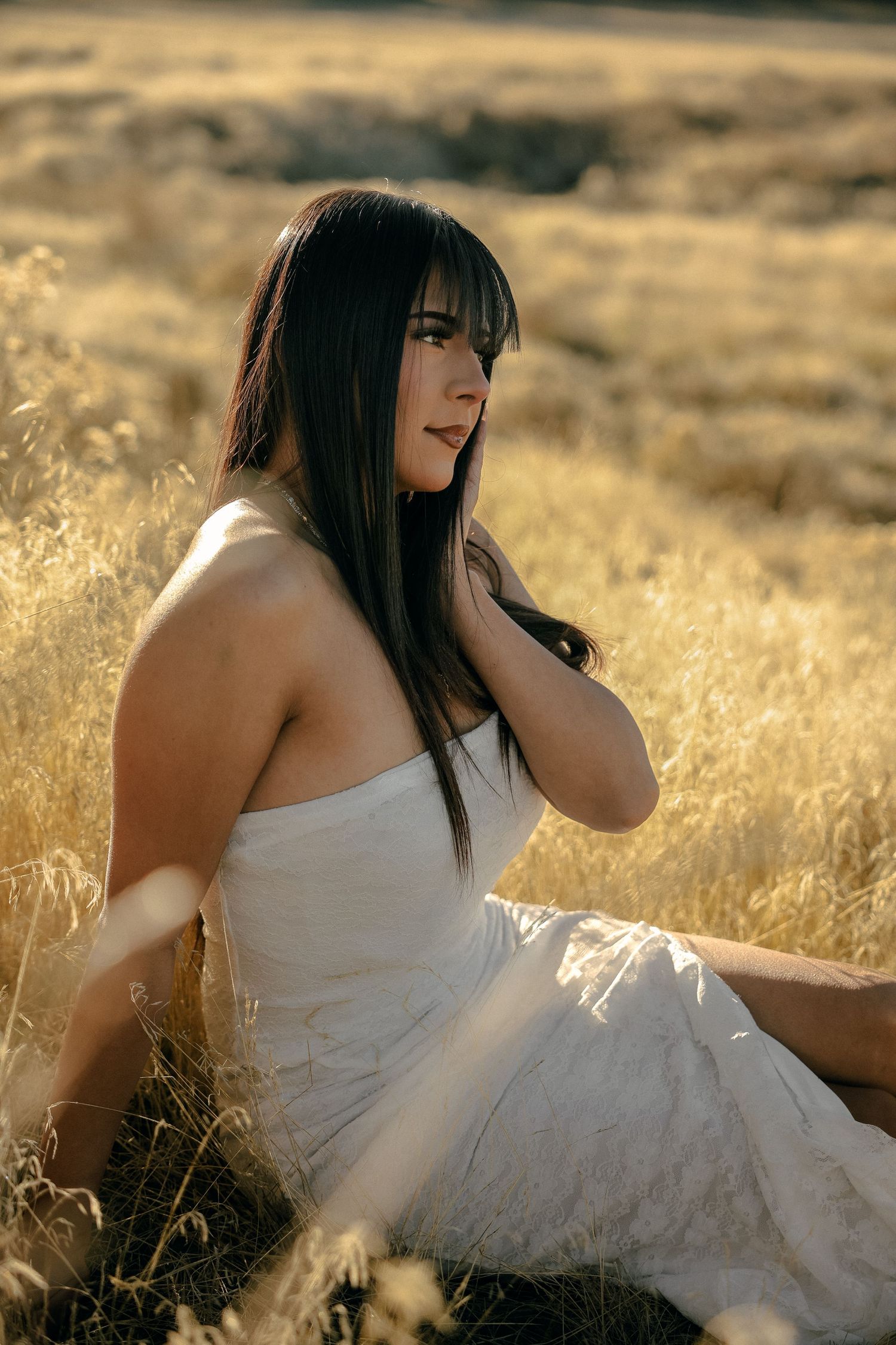 Woman in white dress sits gracefully in golden field during sunset.