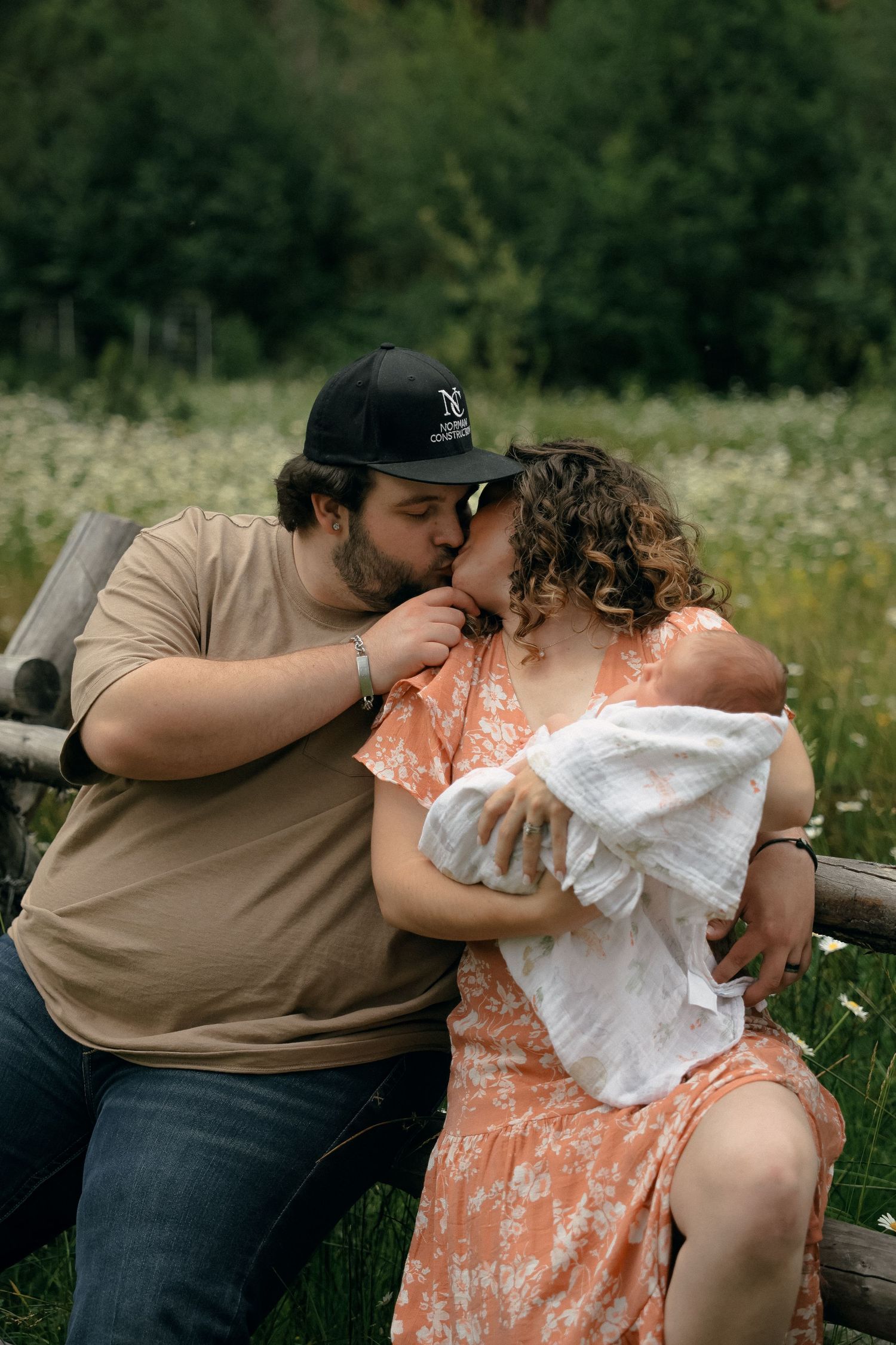 A couple sits on grass and shares an intimate moment in a field on a sunny day.