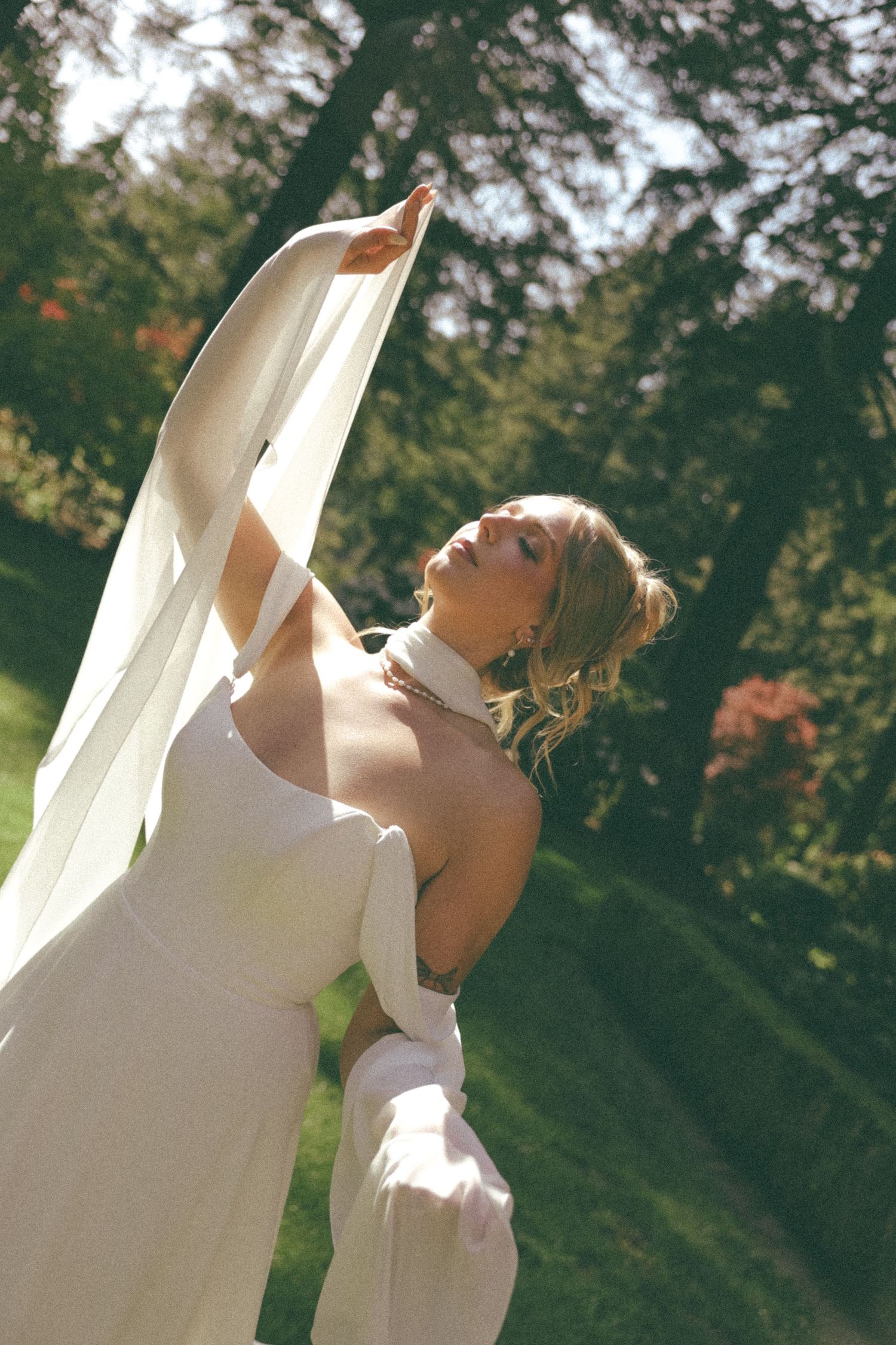 A dreamy sunlit portrait with flowing white fabric against a natural garden backdrop.