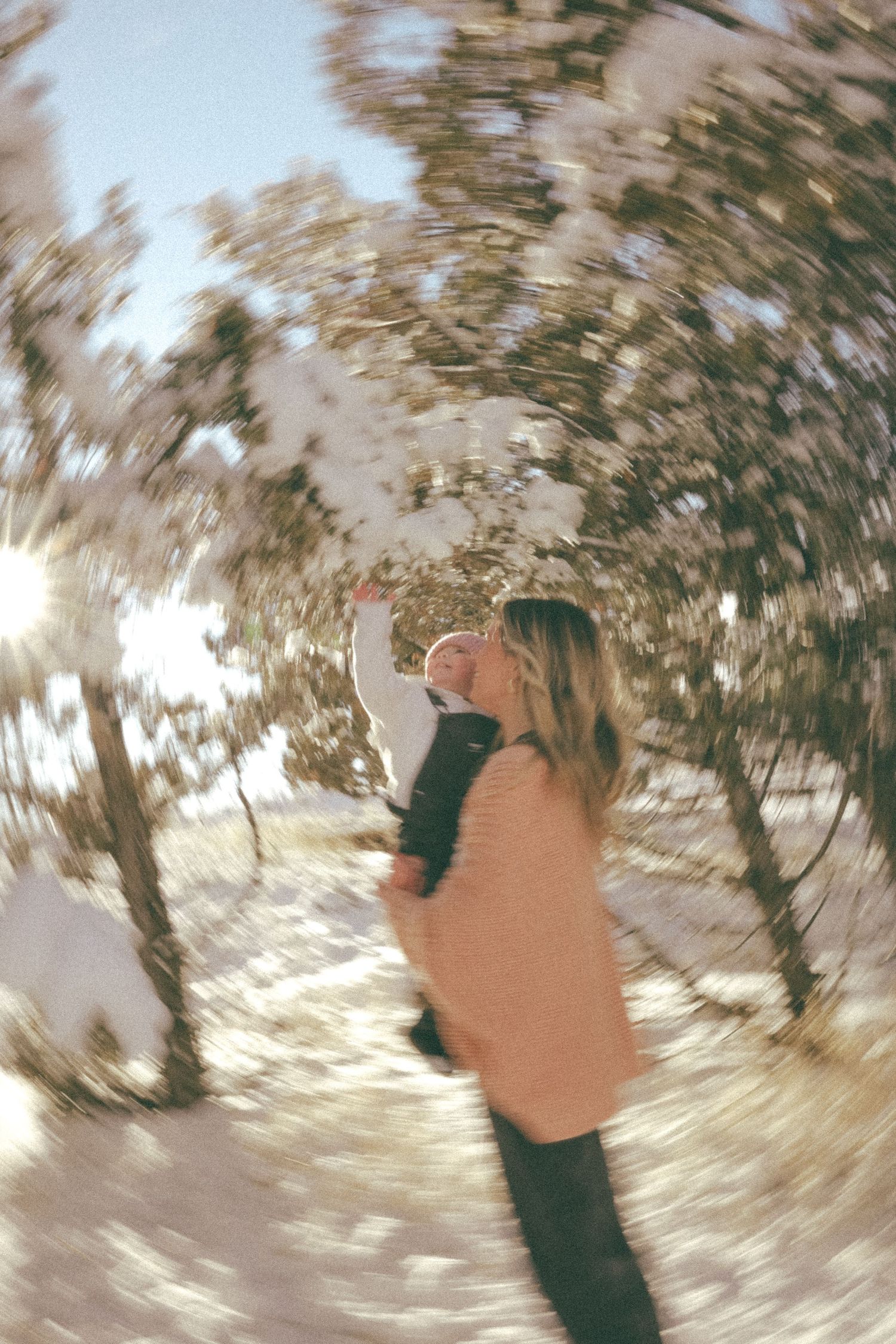 A dreamy fisheye perspective of someone lifting a child in a snowy winter landscape.