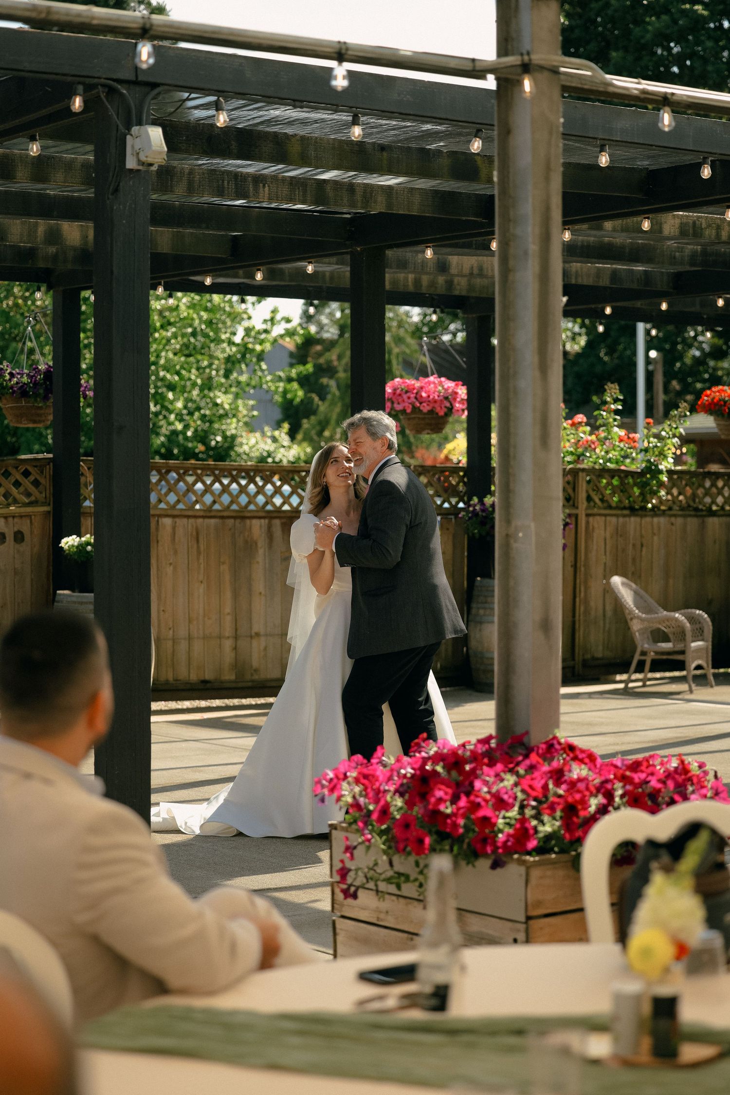 Wedding couple dancing under wooden pergola decorated with string lights.