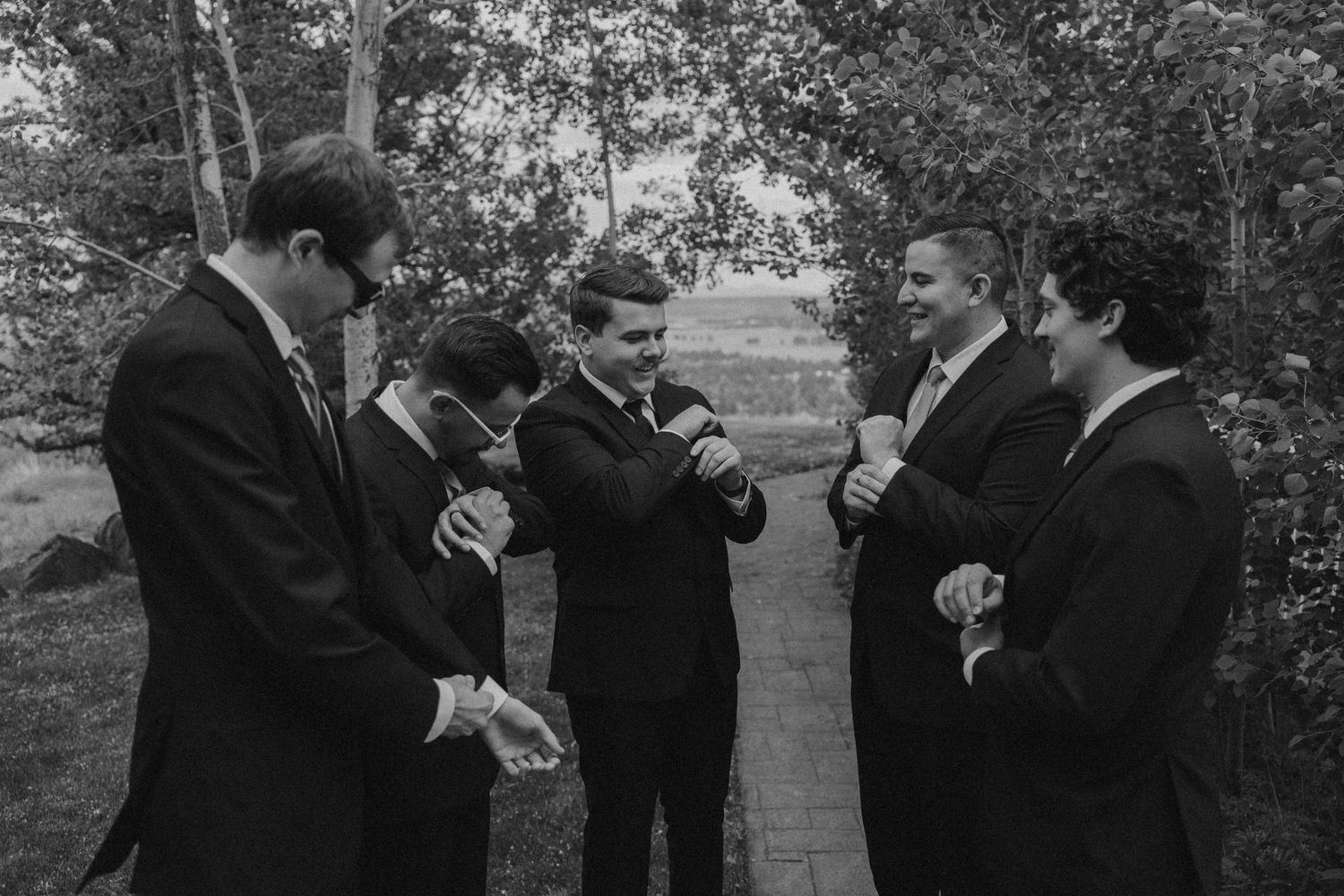 Groomsmen in black suits sharing laughs during wedding day preparations.