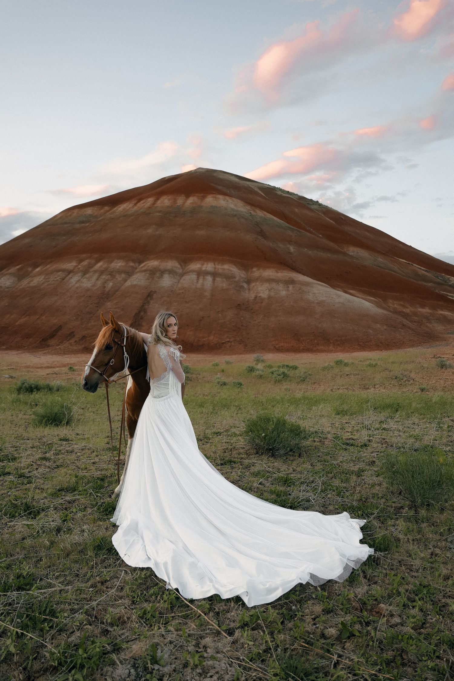 Wedding dress train flowing dramatically against red rock formations at sunset.