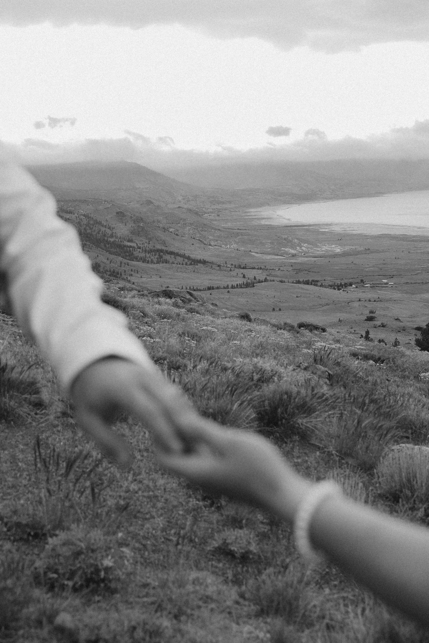 Two hands reaching for each other against a scenic mountain landscape overlooking a misty valley below.