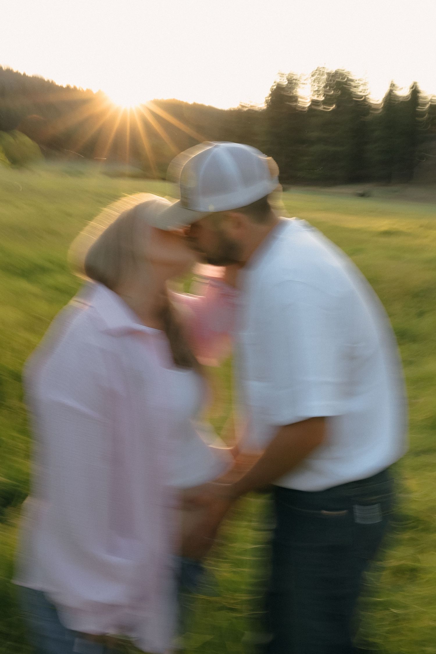 Motion-blurred couple in white shirts embrace in a sunlit grassy field at sunset.