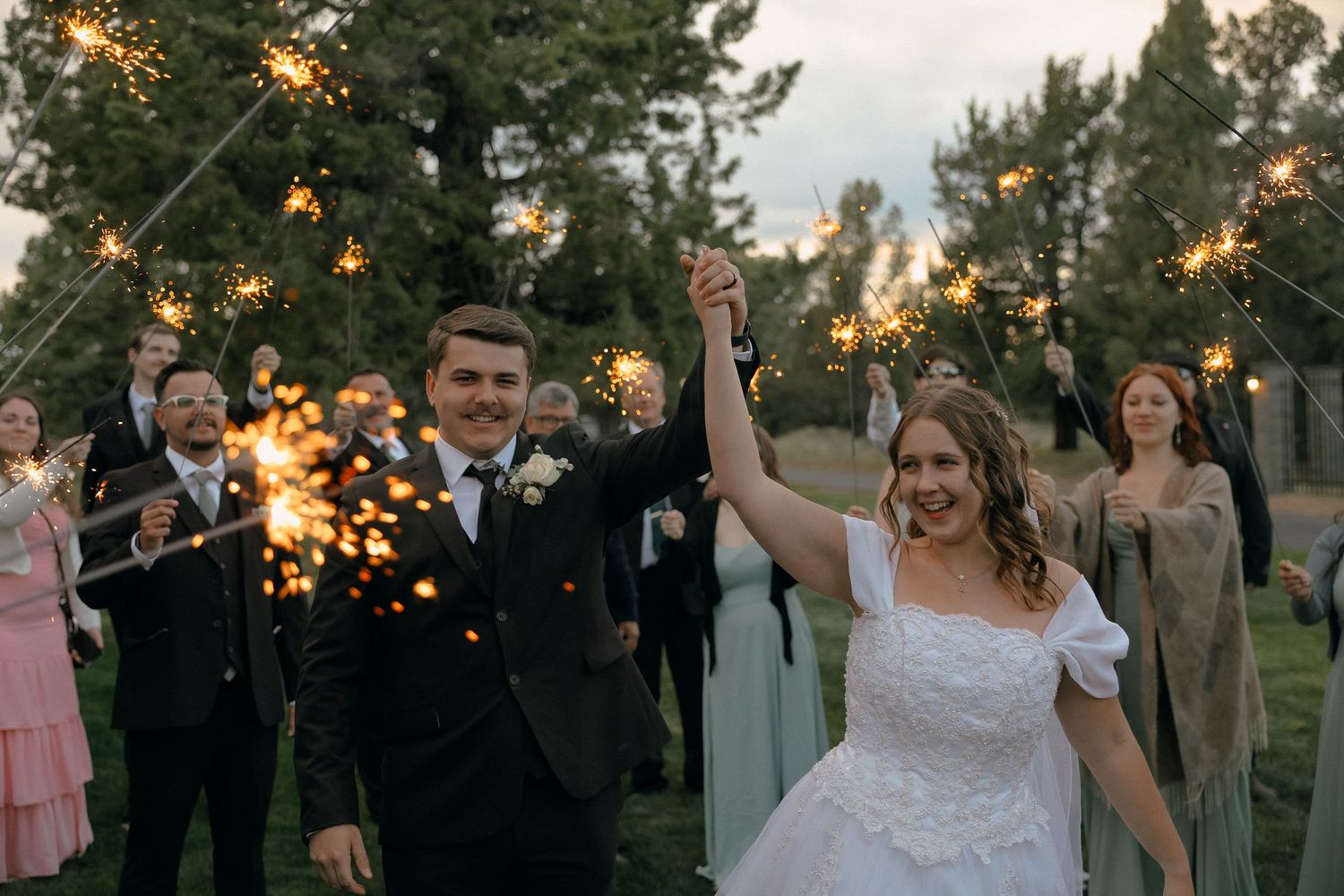 Wedding couple celebrating with sparklers surrounded by guests at outdoor evening celebration.
