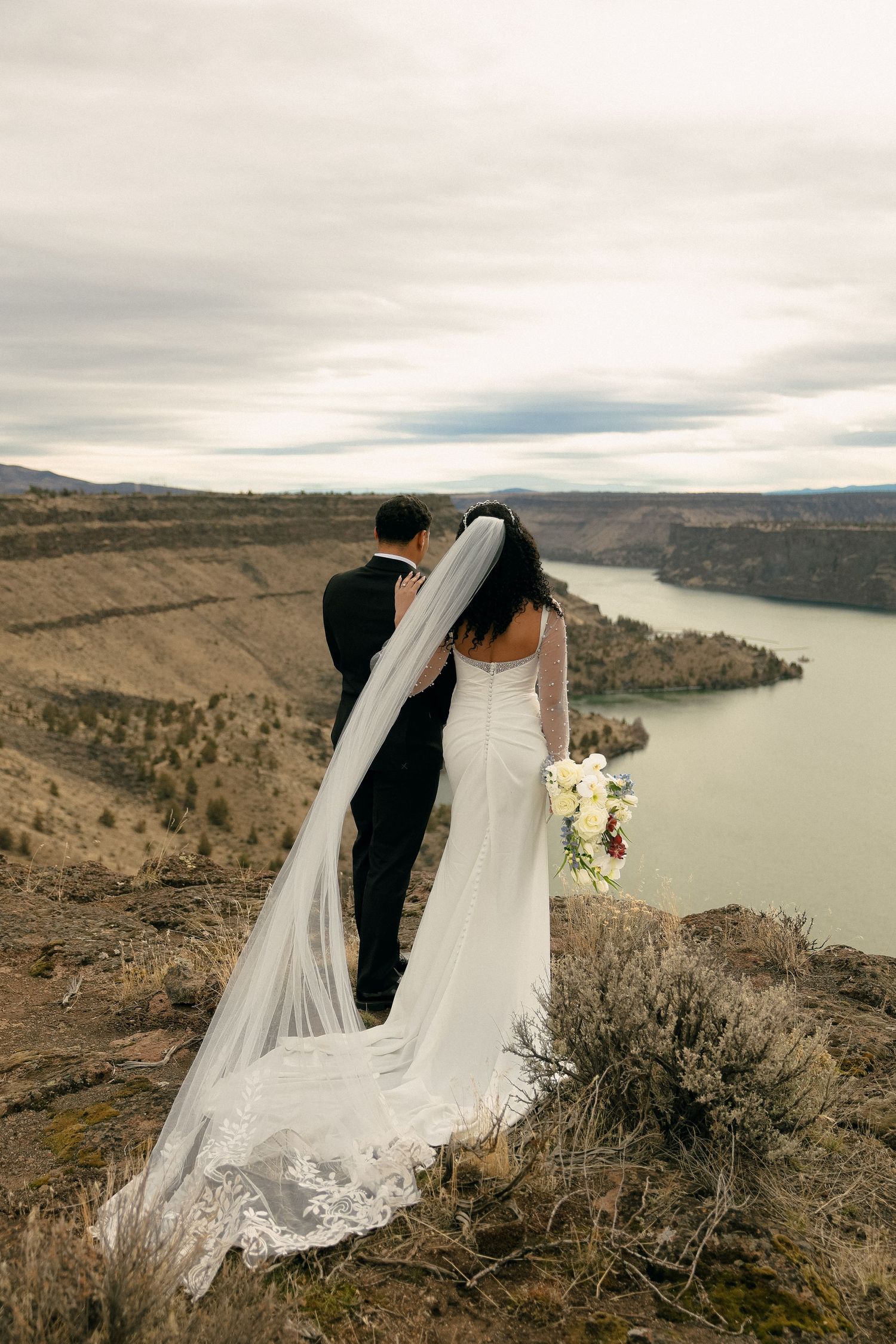 Newlyweds overlooking scenic canyon landscape with long flowing veil.