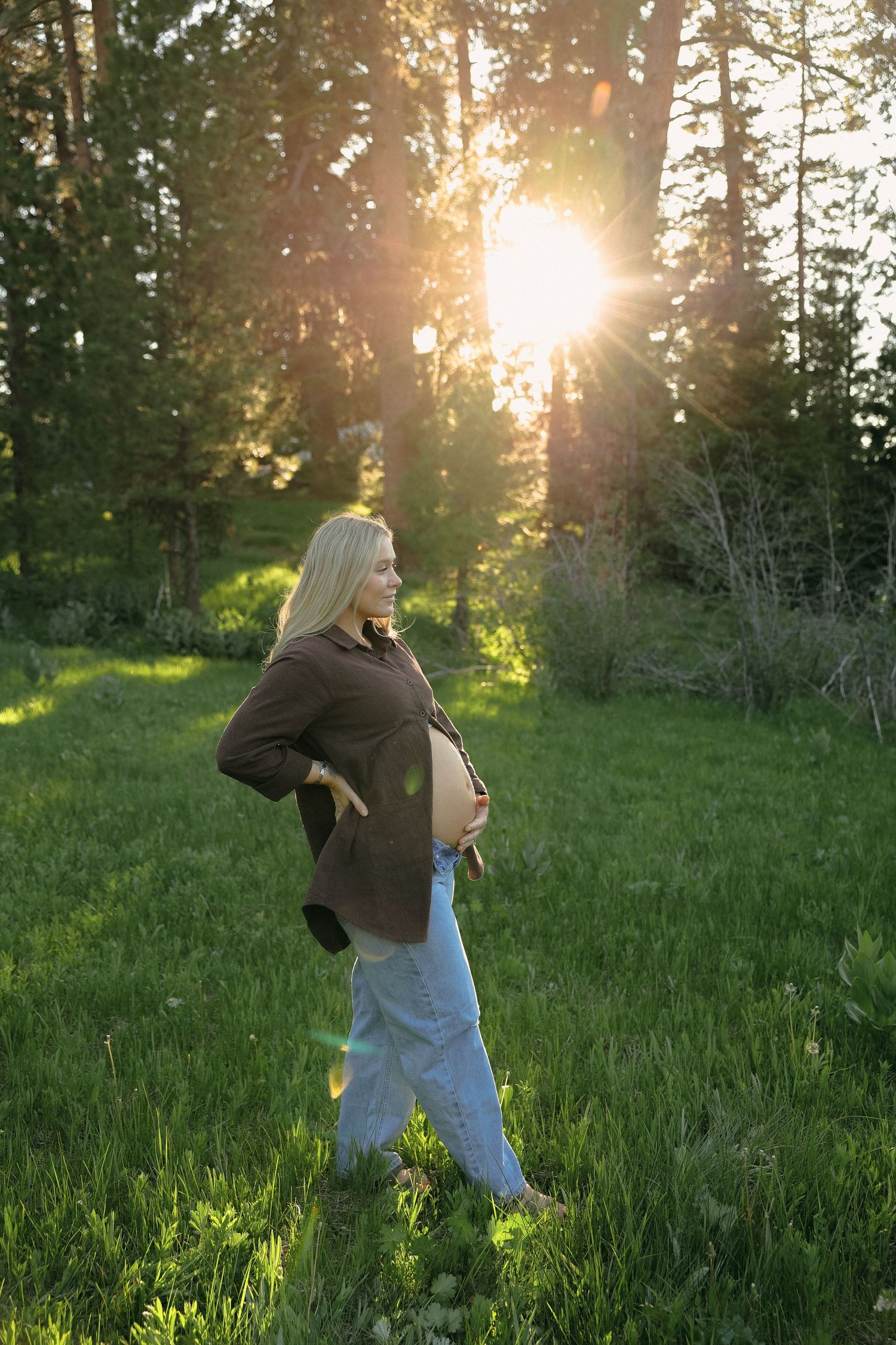 A person dancing in a grassy field during golden hour with sunlight streaming through trees.