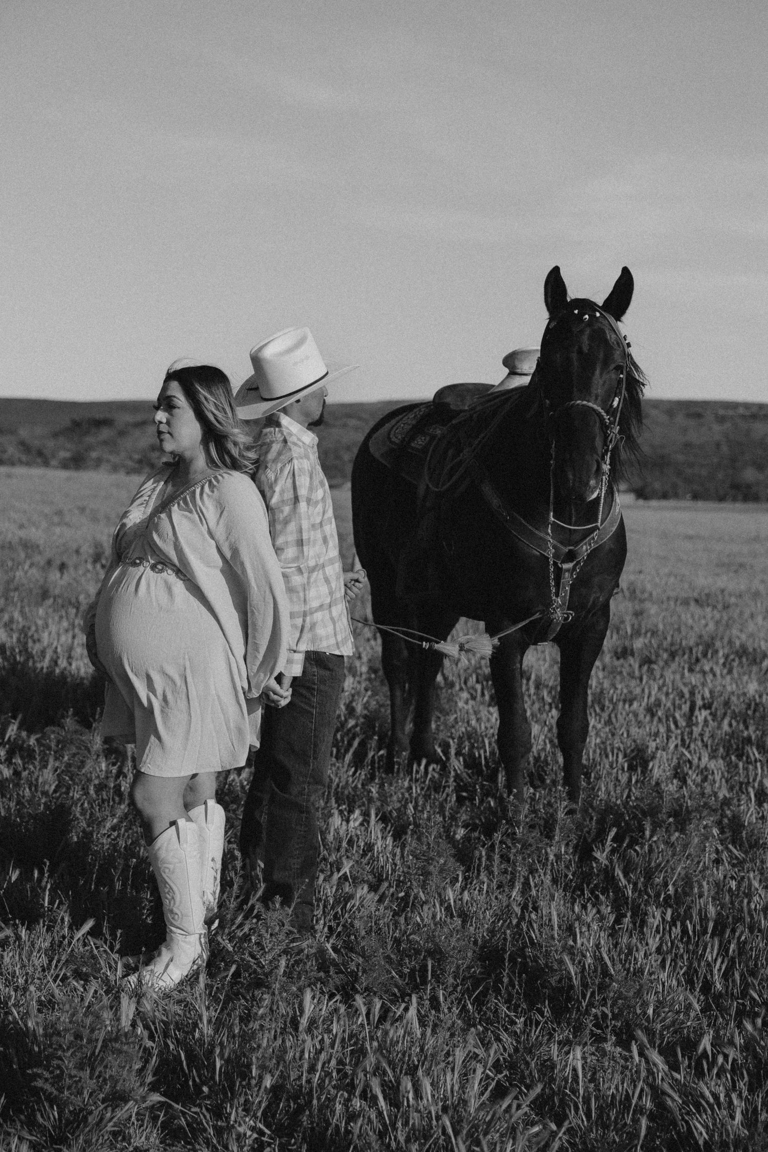 Black and white photo of couple with horse in rustic field setting.