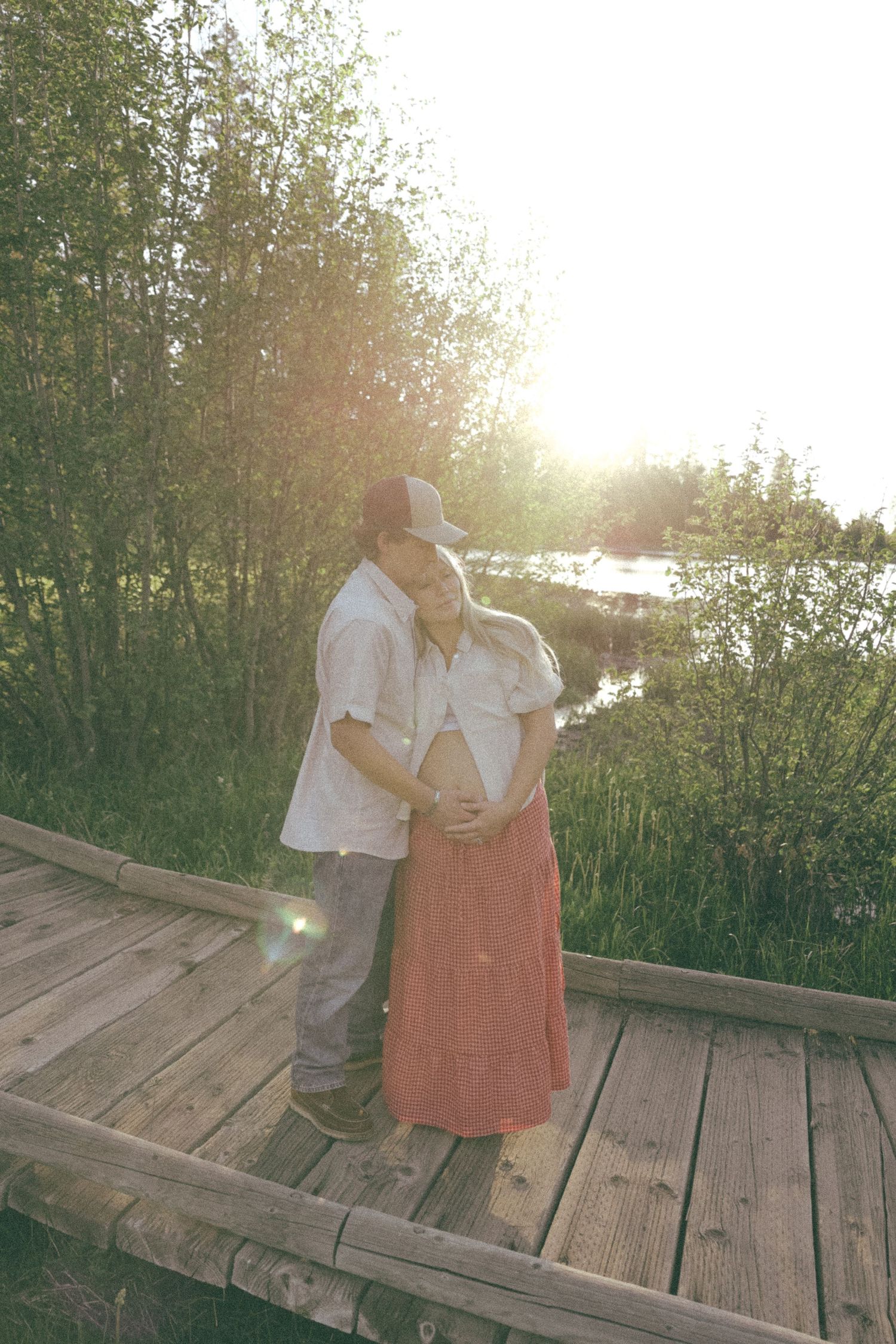 A couple shares a tender moment at sunset on a wooden deck surrounded by greenery.