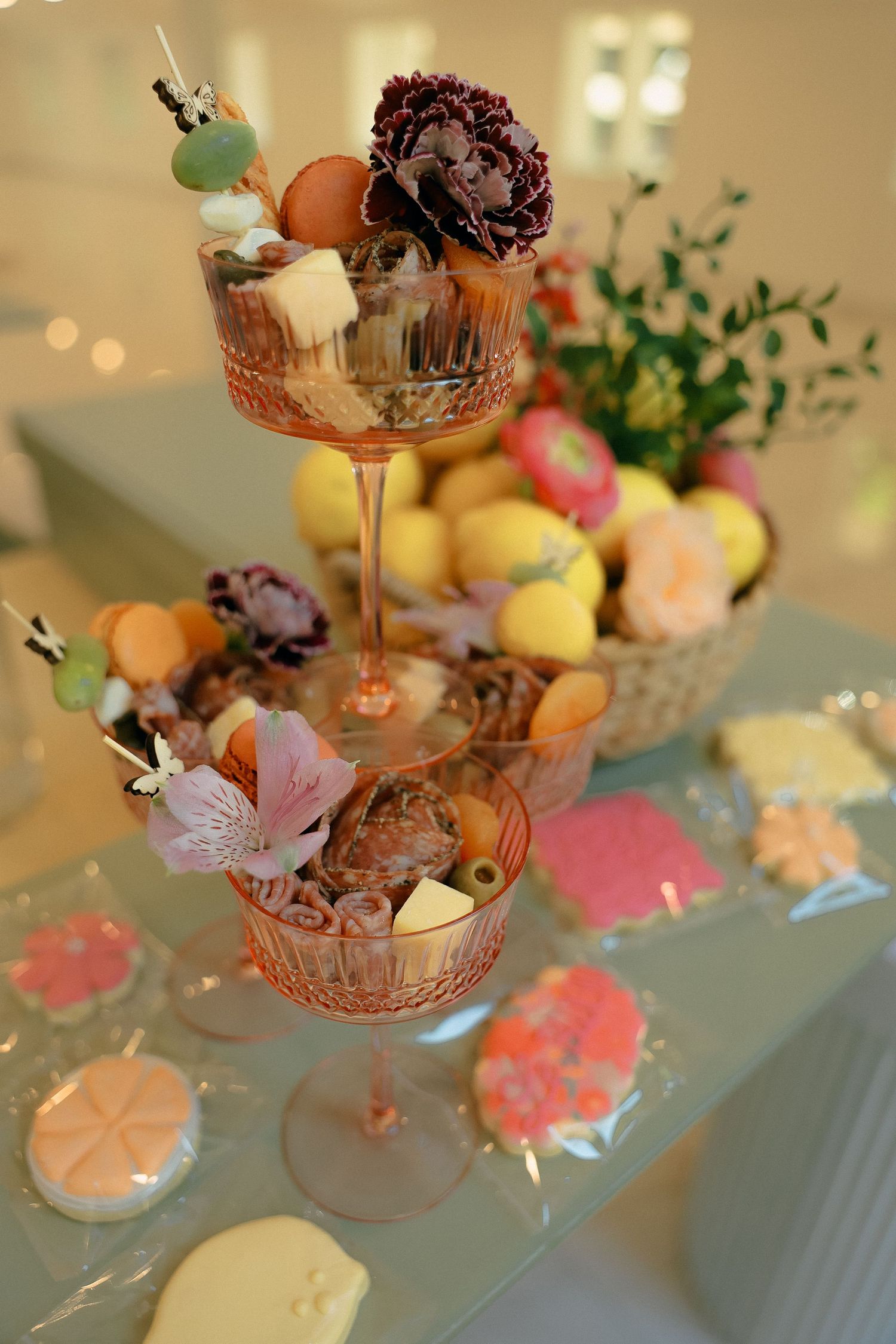 Decorative tiered cocktail glasses filled with colorful macarons and floral arrangements.