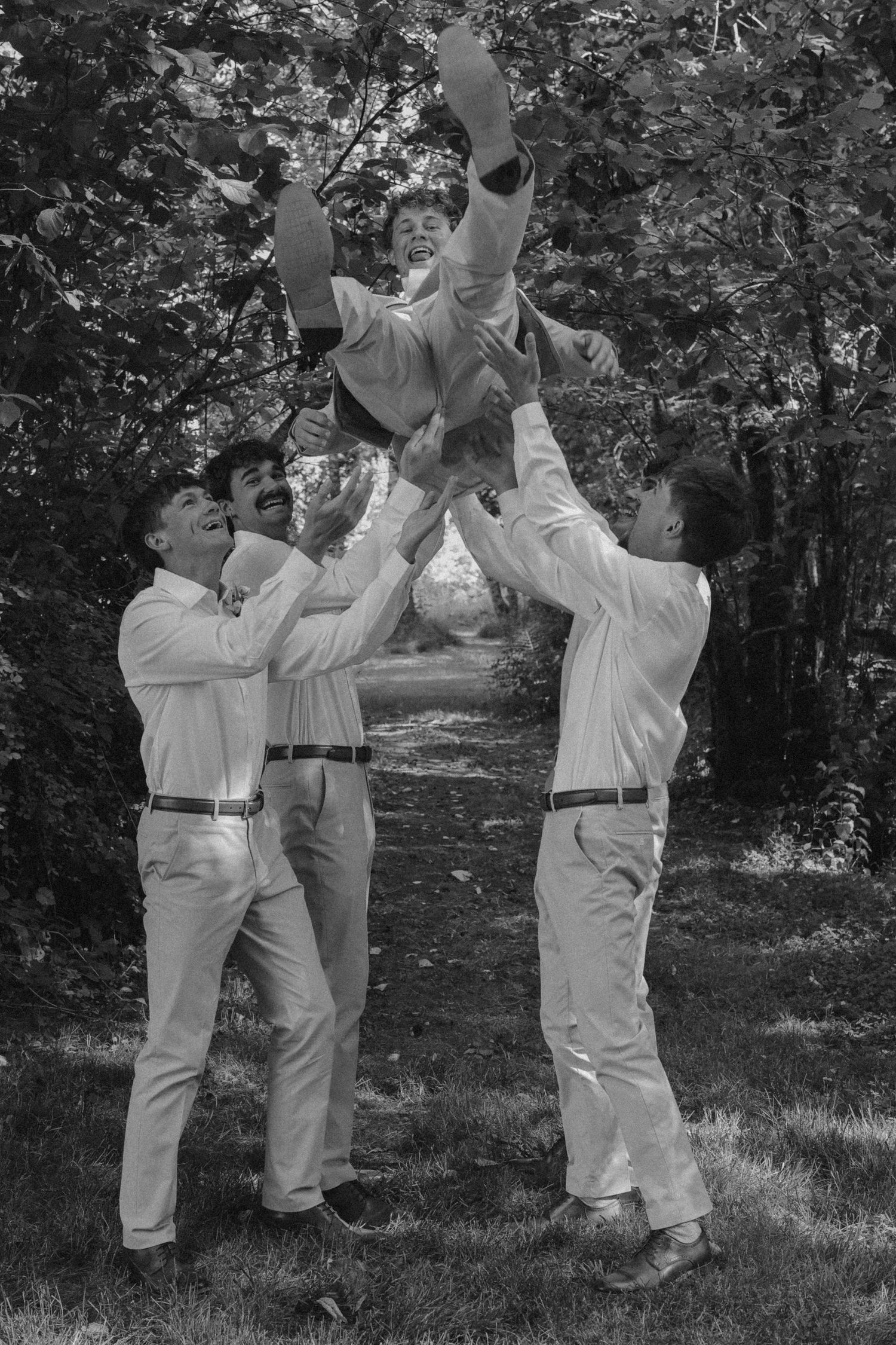 Three men in matching white outfits perform a synchronized dance routine in a grassy outdoor setting.