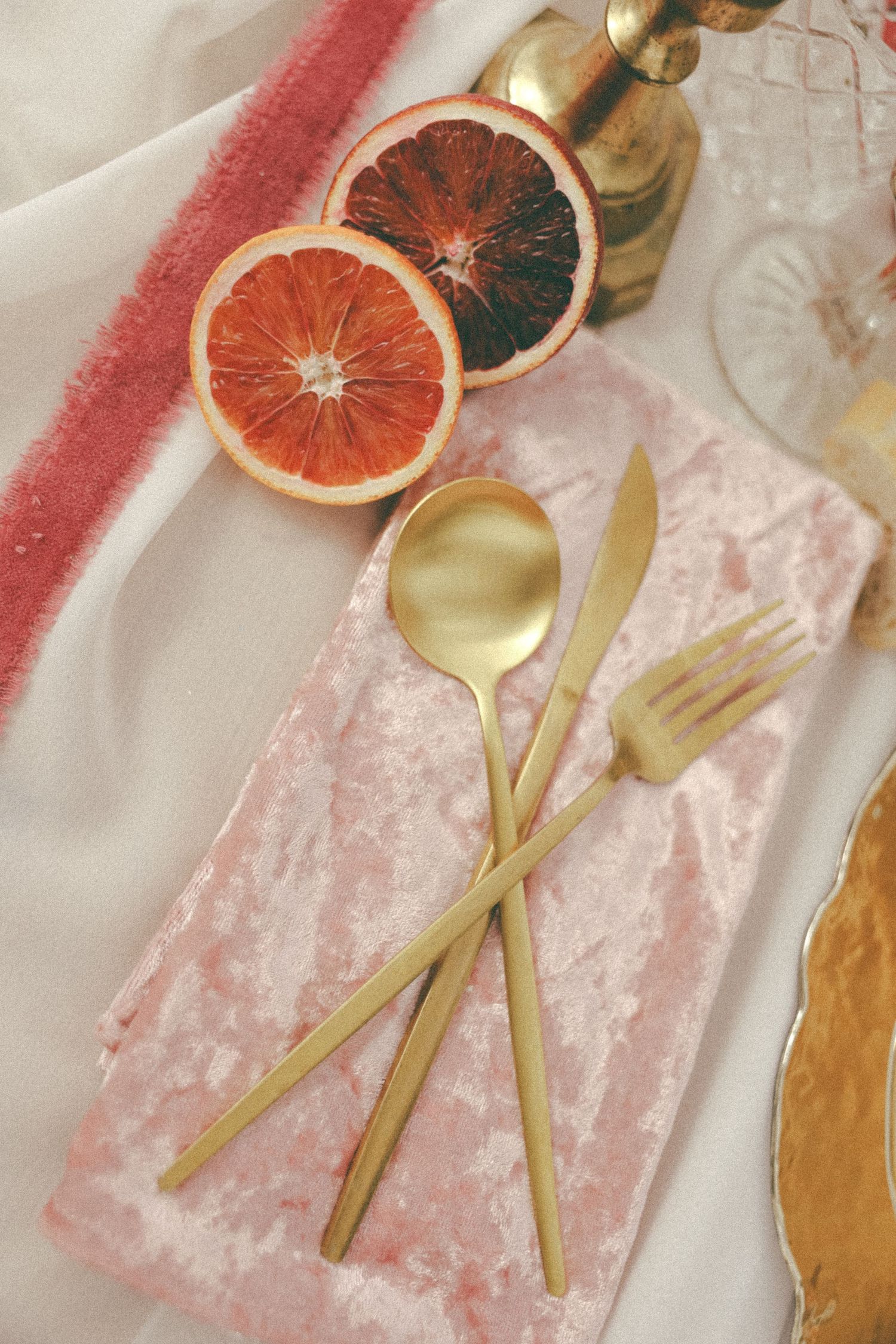 Wedding table setting details with gold cutlery, grapefruit slices, and pink velvet.