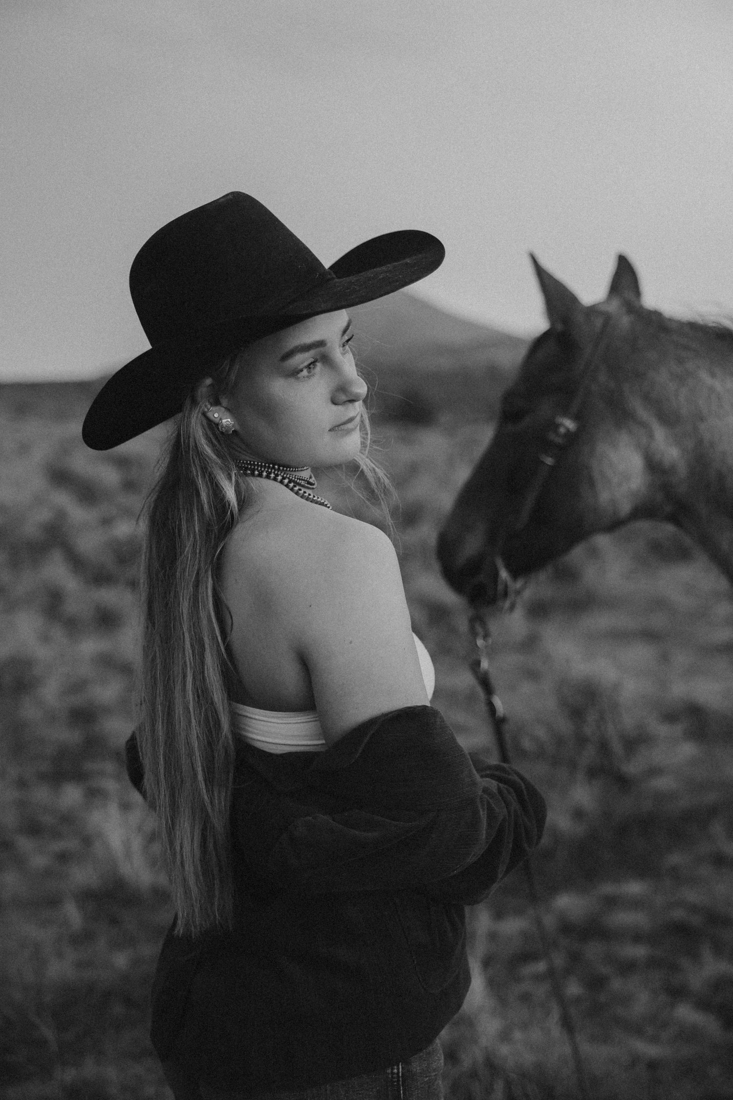 Moody black and white portrait with person in cowboy hat and horse silhouette.