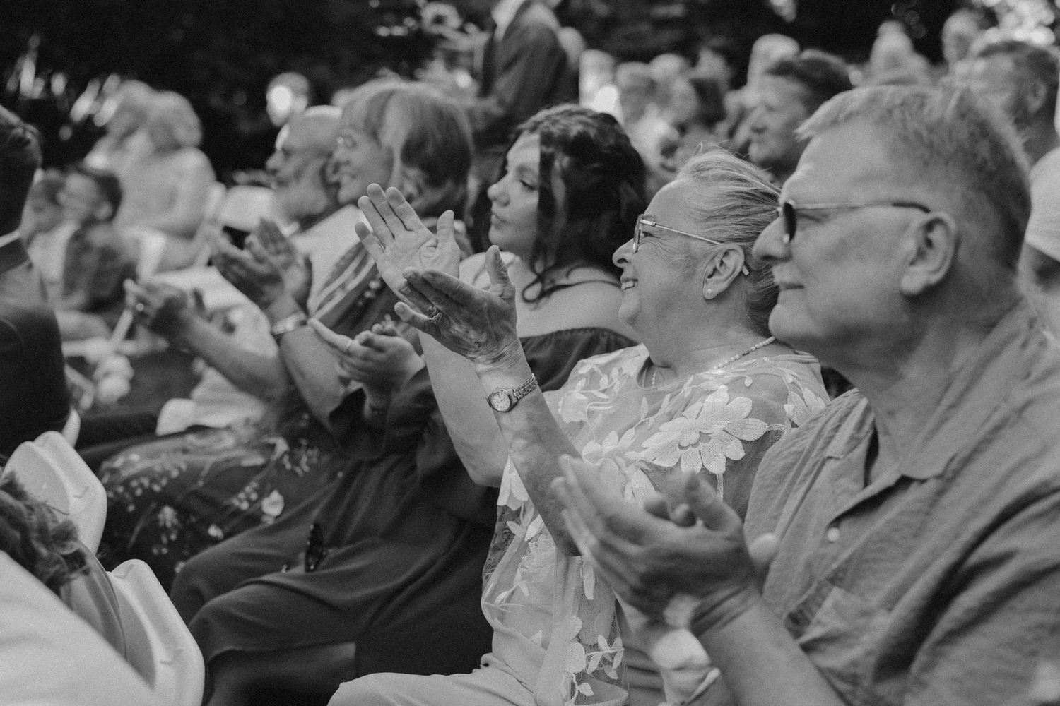 A crowd of elderly spectators sit in stadium seats raising binoculars to their eyes during an event.